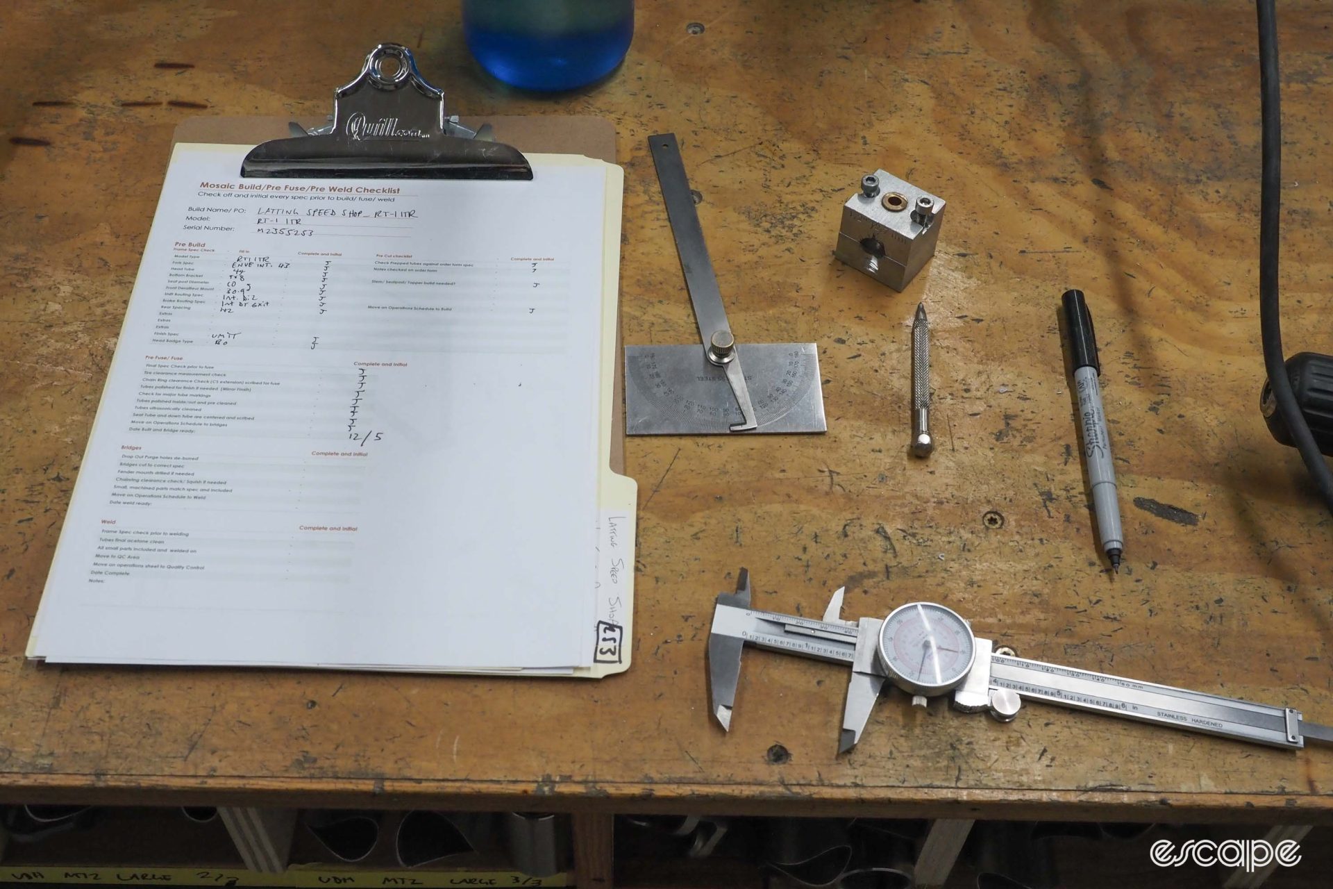 A set of calipers and other tools sits on a bench alongside a customer order sheet.