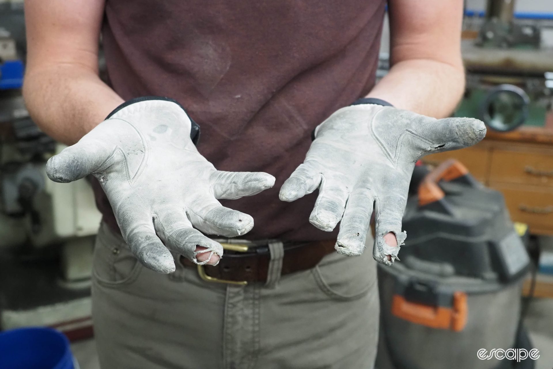 Aaron Barcheck holds his hands out to show weathered gloves with holes in several fingers.