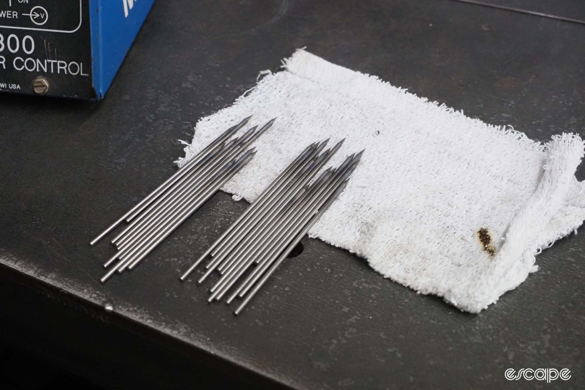 Two piles of tungsten electrode rods sit on a rag on a bench.