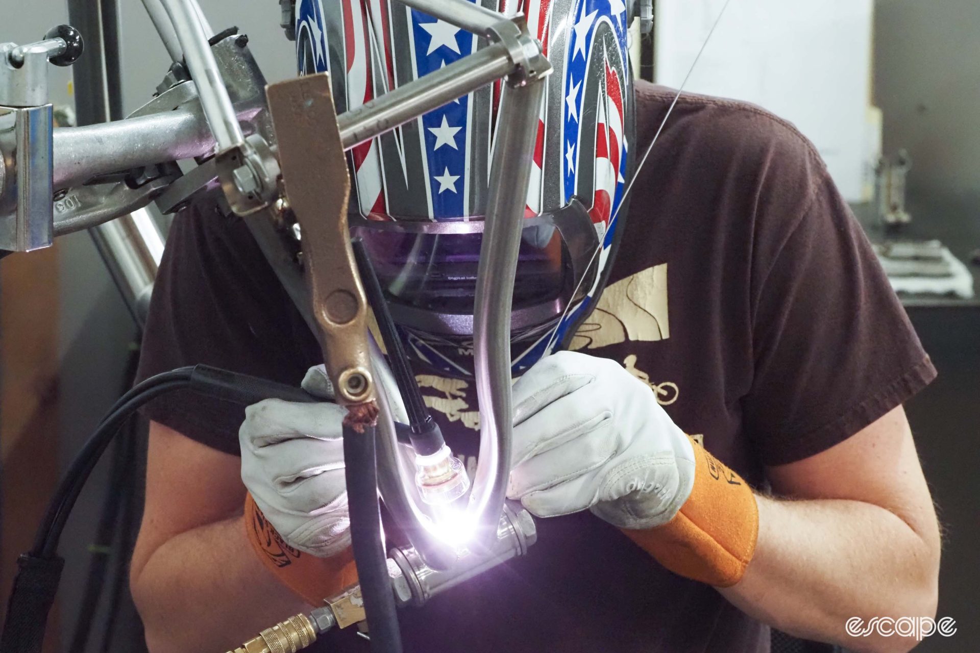 Another view of welding the bottom bracket, showing the welder with a torch in one hand, welding rod in another.
