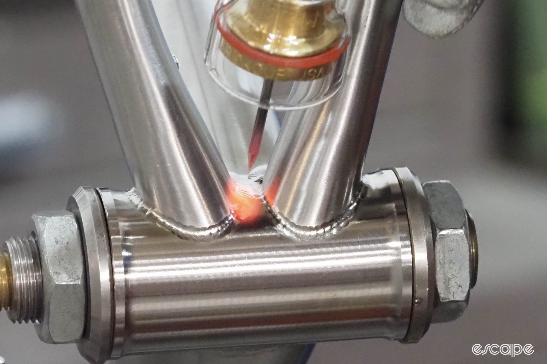 A fusion weld on a bottom bracket. The welds are puddled but raw, and the frame glows red where the chainstay meets the bottom bracket shell as the welder passes.