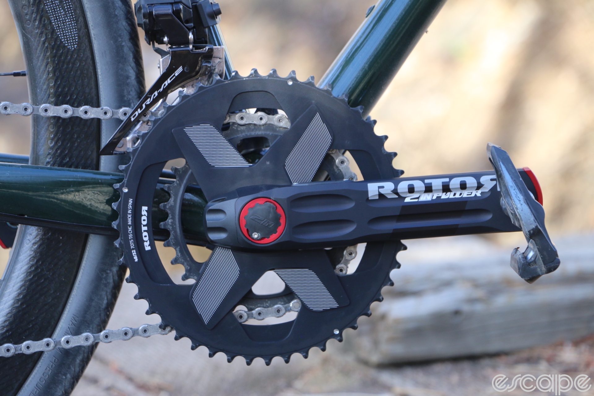 Rotor's 2InPower driveside crankarm, shown on a bike. The arm is level and the black arm features red accents at the bottom bracket and end of the arm. The chainrings are on an X-shape spider.