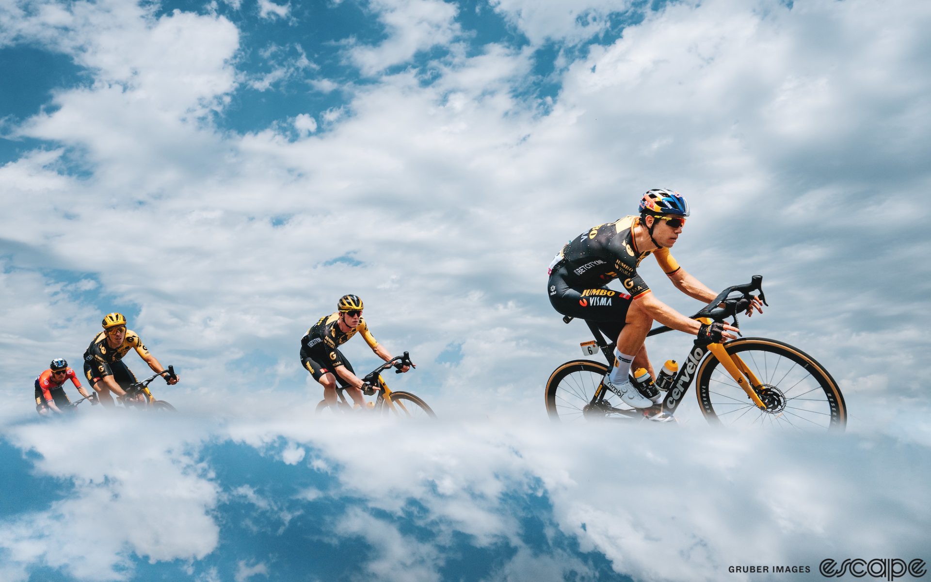 Wout van Aert leads the Jumbo team on a descent at the Tour de France. He leans into the turn and is framed against a blue sky half-covered in white clouds, which are reflected below his bike in the bottom third of the image to make it seem like he's floating in the air.