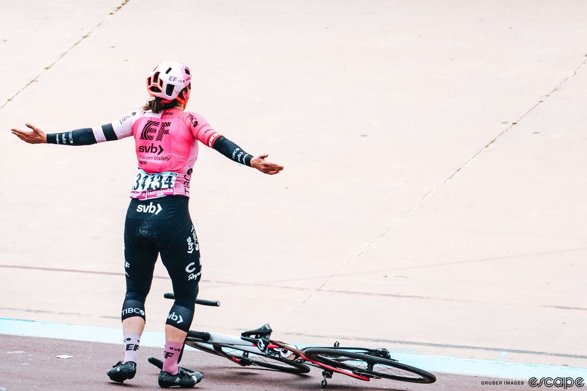 Alison Jackson holds her arms wide as she drops her bike in the Roubaix velodrome after winning the 2023 Paris-Roubaix in a sprint. Her gesture is one of showmanship and disbelief.