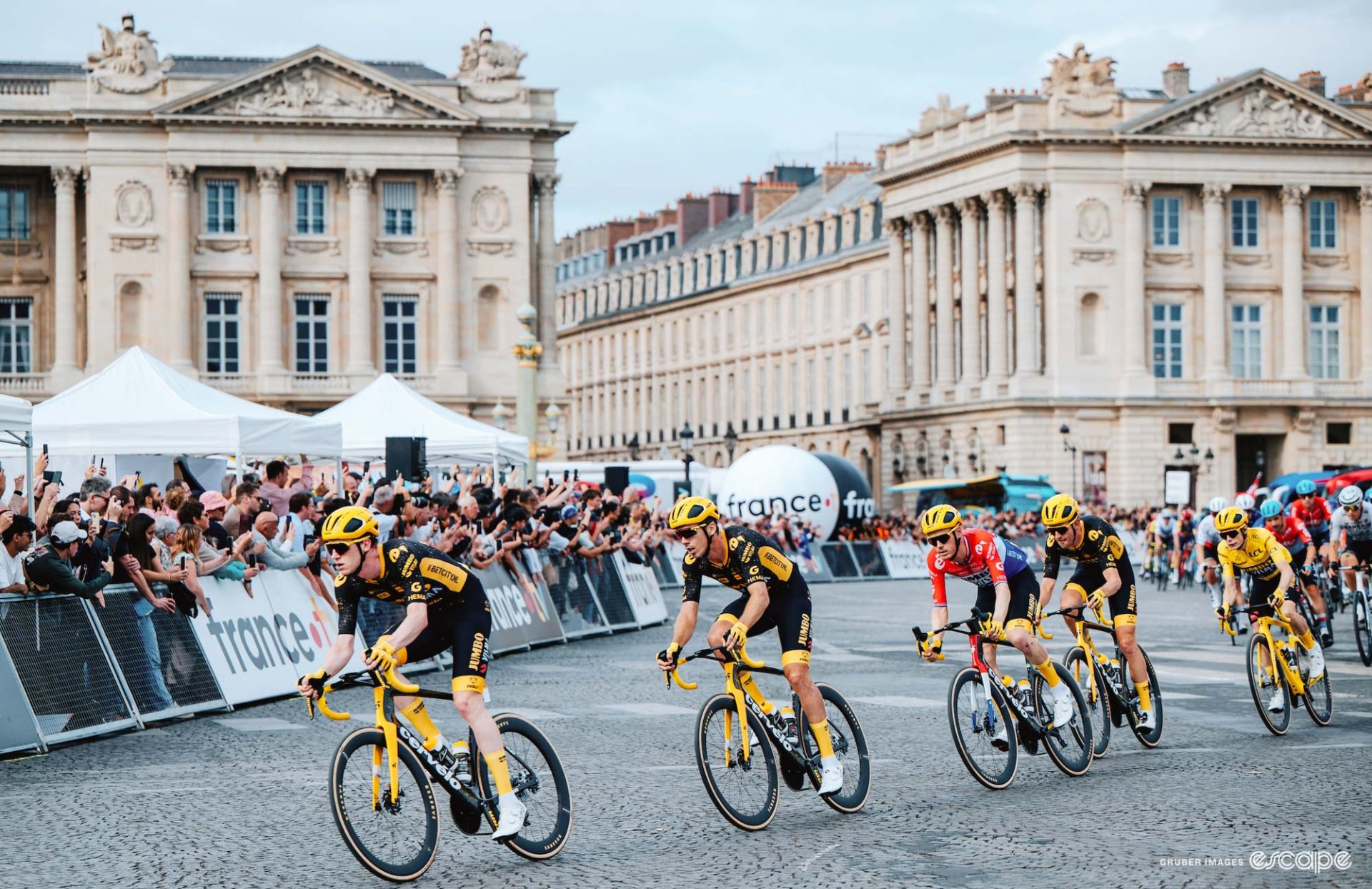 Nathan van Hooydonck leads the Jumbo-Visma onto the Champs-Elysées in the Tour de France. Christophe Laporte, Dylan van Baarle, and Tiesj Benoot follow while at the back of the line, Jonas Vingegaard is shown in the yellow jersey.