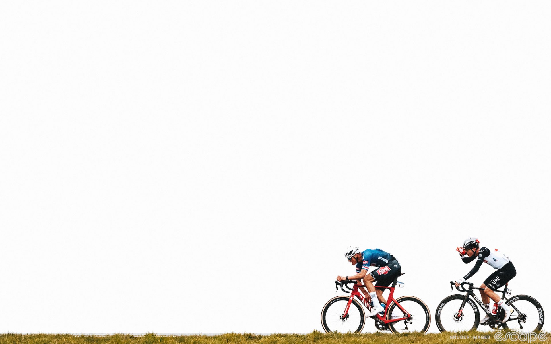 Mathieu van der Poel leads Tadej Pogačar through a flat field at the Tour of Flanders. They're shown against a blown-out white sky, with heavy contrast.