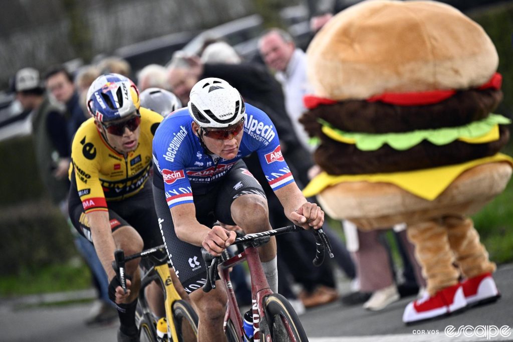 Mathieu van der Poel leads Wout van Aert at the 2023 E3 Saxo Classic. On the road is a person dressed as a large hamburger.