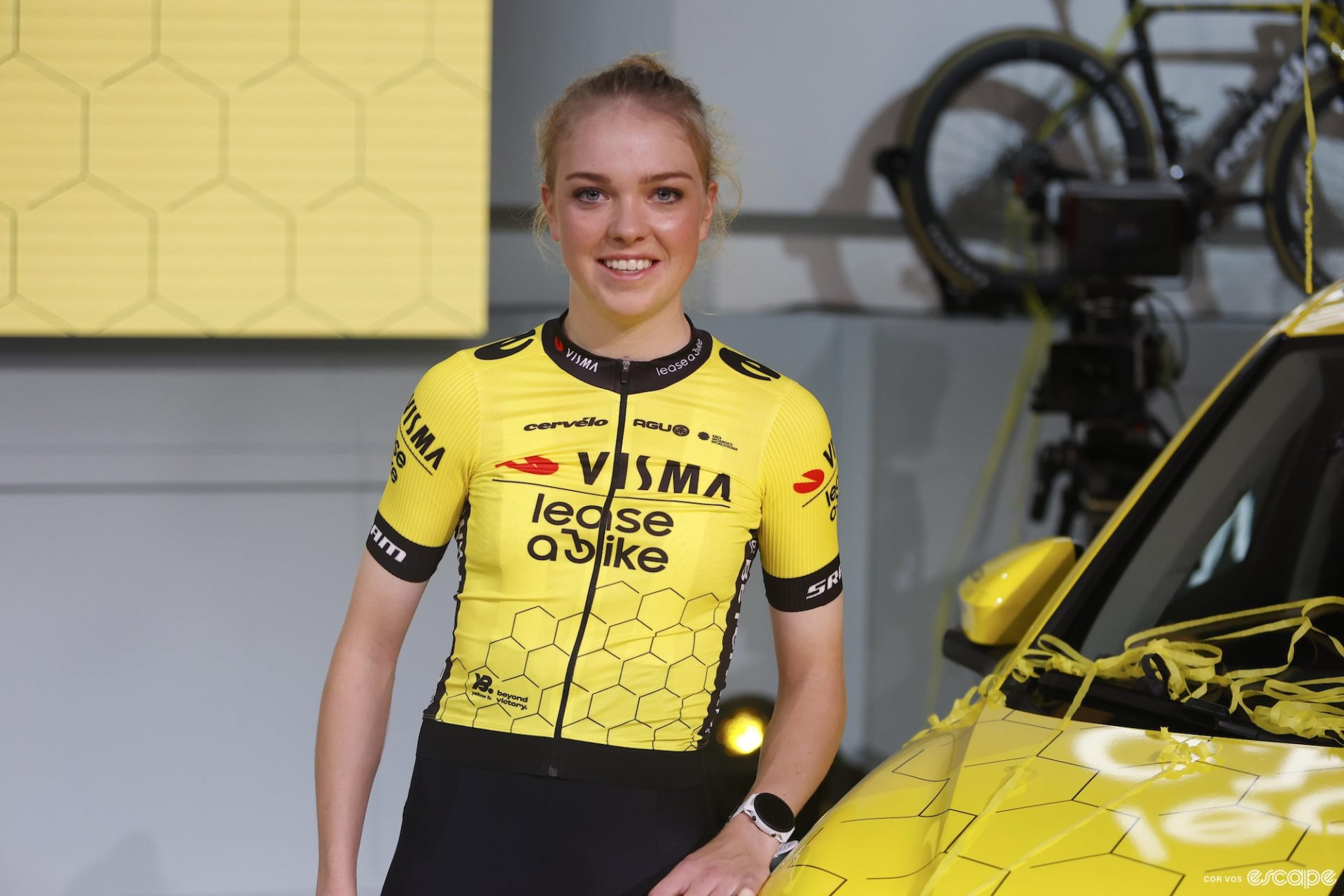 Fem van Empel leans on the hood of a car in the new Visma-Lease a Bike kit. The simple jerseys are yellow with black logos and a geometric honeycomb pattern on the lower half.
