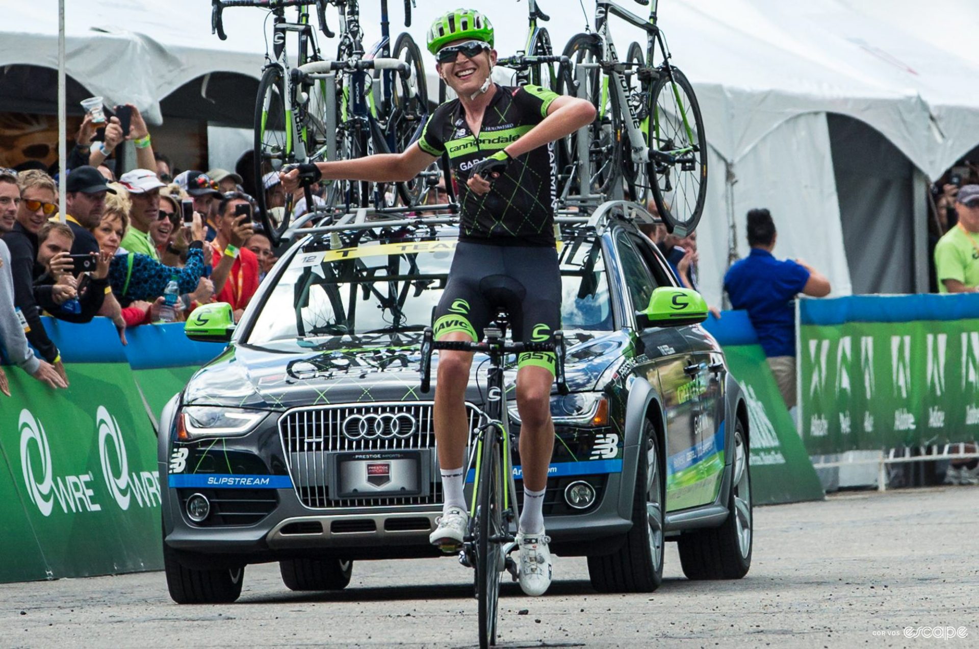 Joe Dombrowski sits up to celebrate as he crosses the line to win the Snowbird stage of the Tour of Utah. His team car is behind him and he has a wide smile on his face.