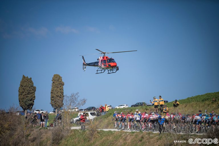 A TV helicopter hovers in front of the peloton at Strade Bianche.