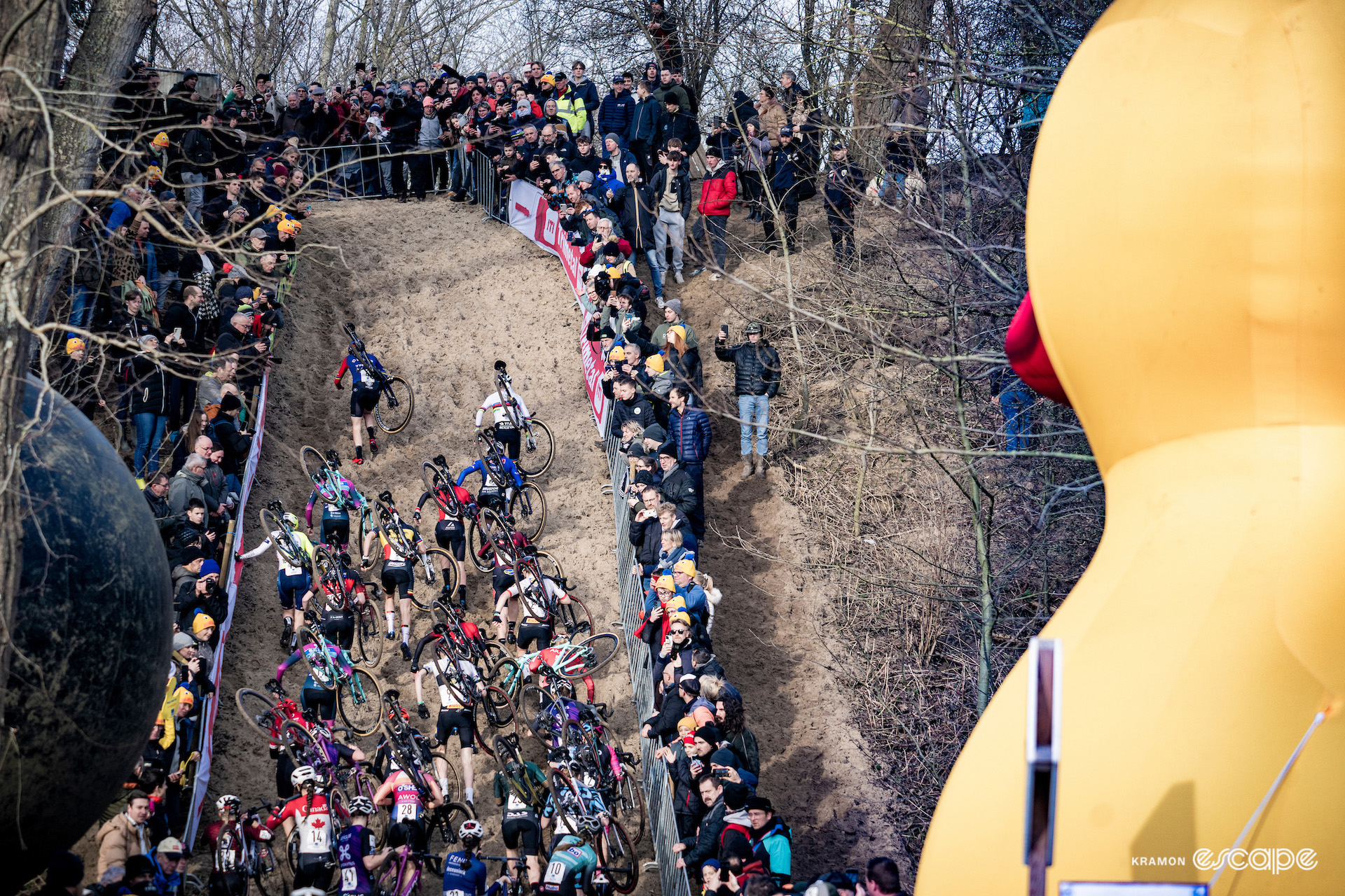 The elite women run up a sand dune early in X2O Trofee Koksijde - Vlaamse Duinencross as a large inflatable duck looks on.