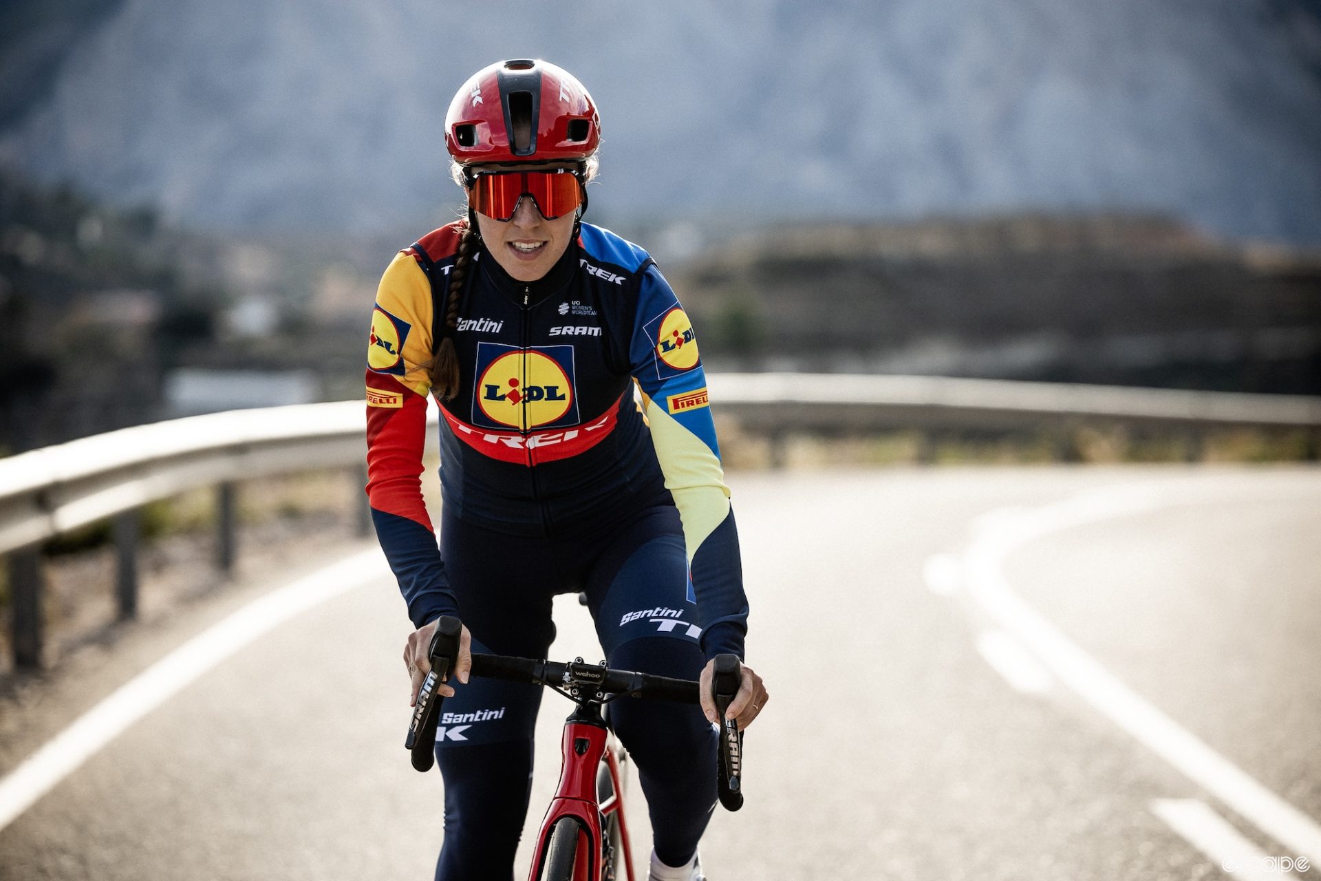 Shirin van Anrooij climbing out of the saddle. Her Lidl-Trek kit features bold blocks of primary colors, with a blue and red body broken up by bright yellow around the distinctive Lidl logo.