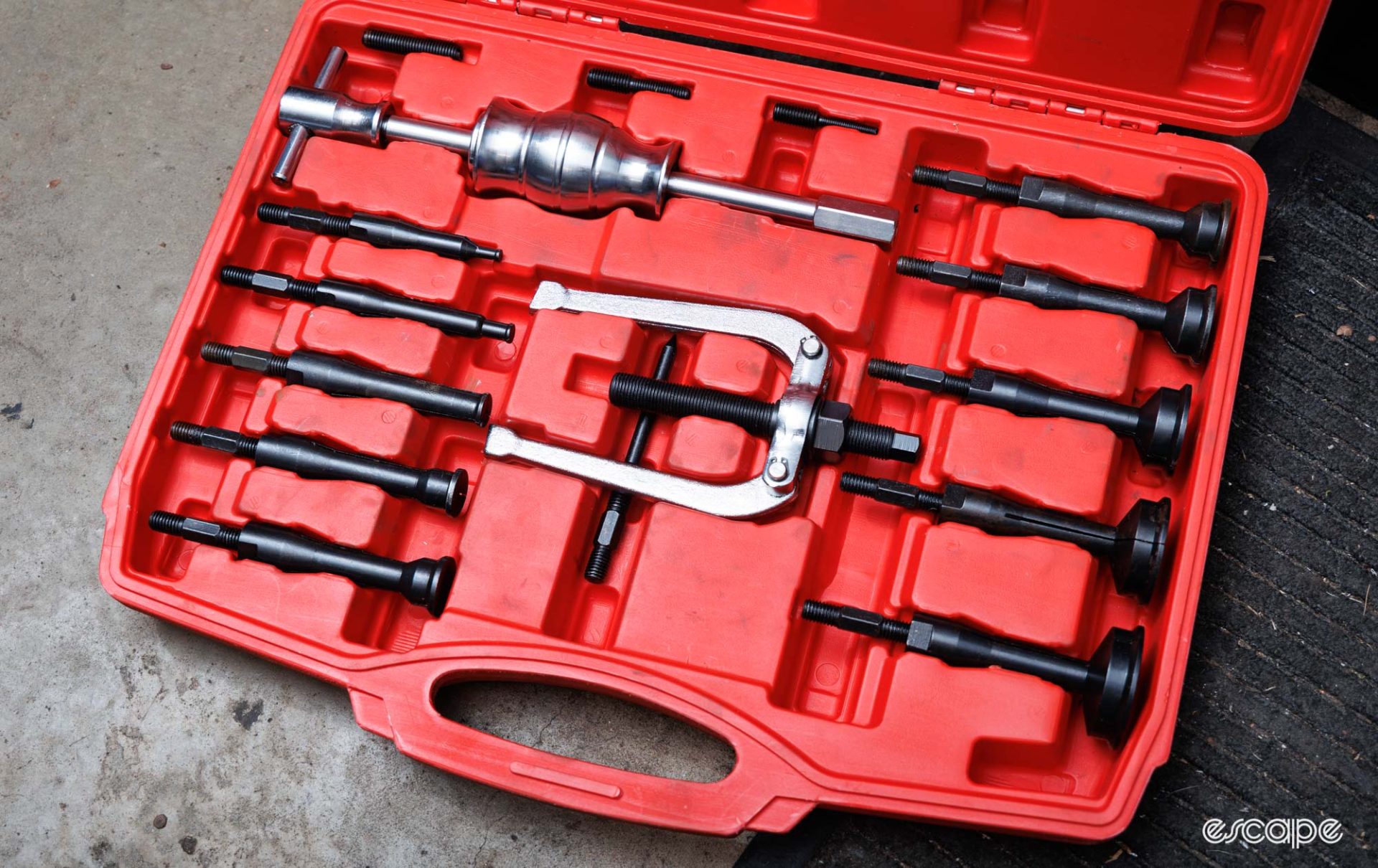 A non-branded blind hole puller kit sits on the floor of a workshop. Many pieces of steel tools are seen. 