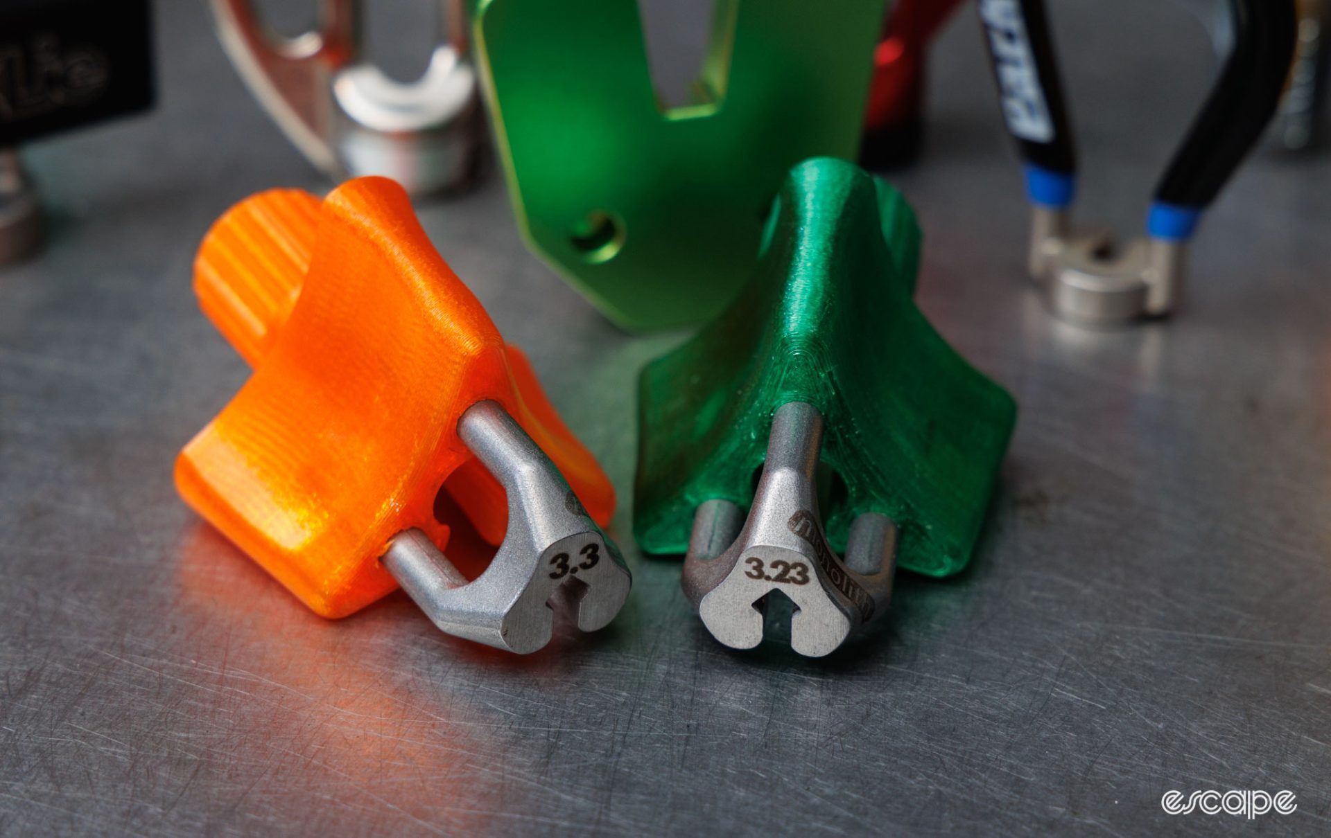 Two sizes of Monolith spoke tool sitting flat on a bench. One is orange and 3.3 mm in size, the other is green and 3.23 mm in size. 