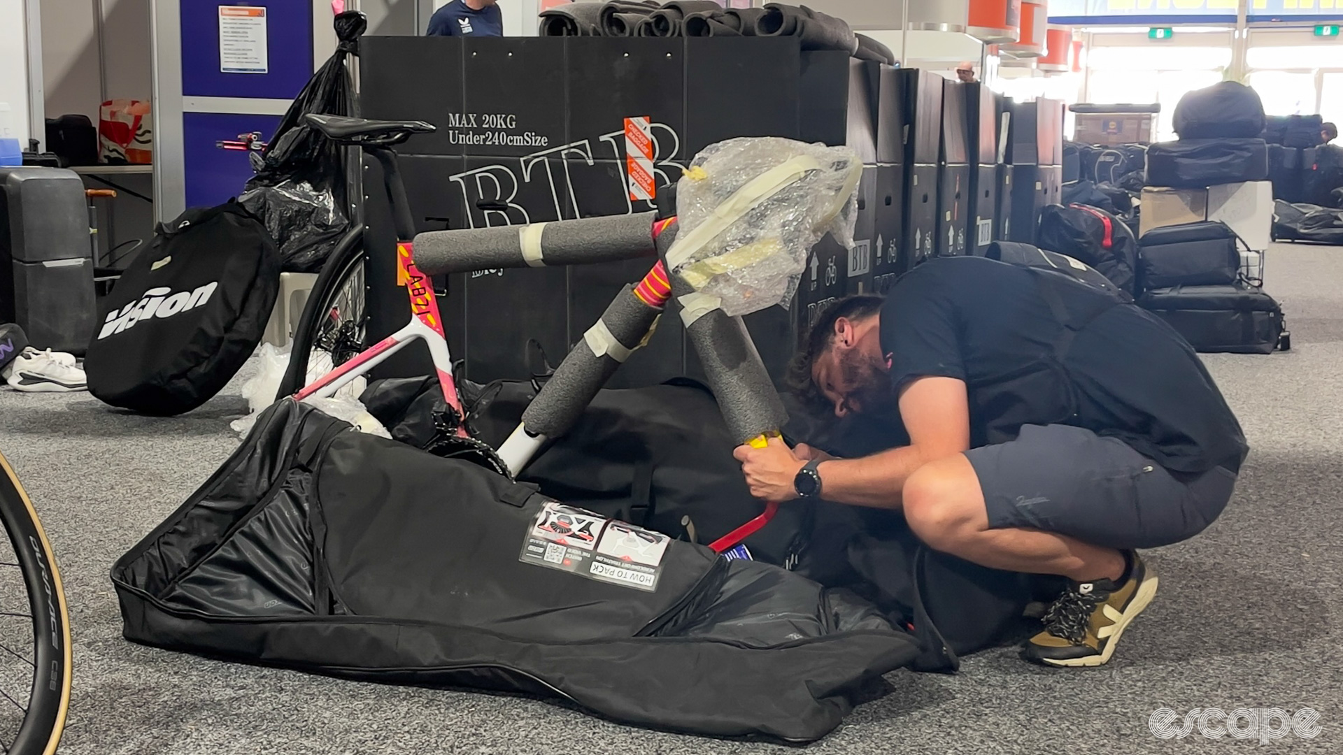 The photo shows a team mechanic wrapping a bike in soft foam and packing it into a bike bag. 