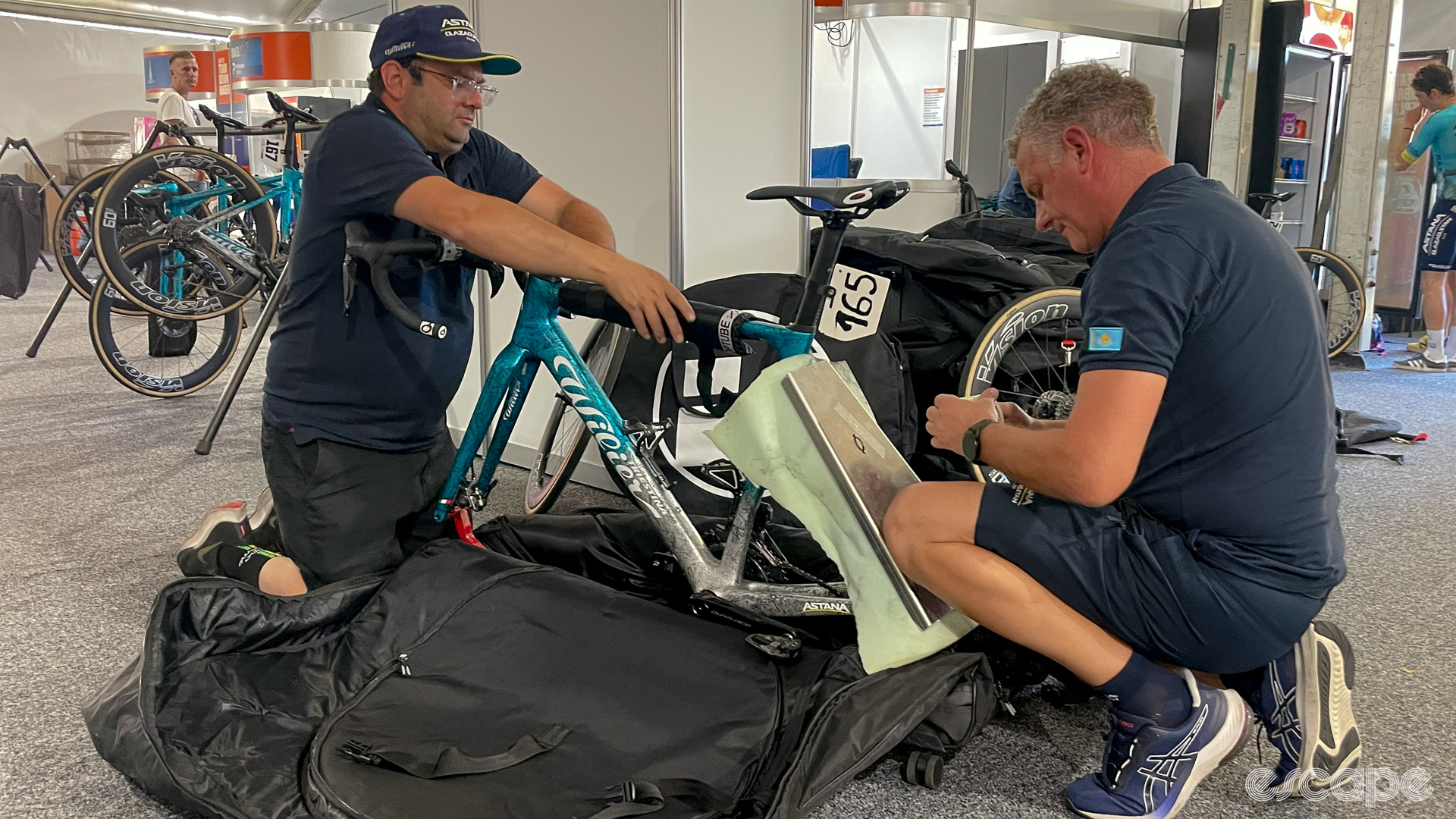 The photo shows two Astana mechanics wrapping a Wilier bike for packing into a bike bag. 