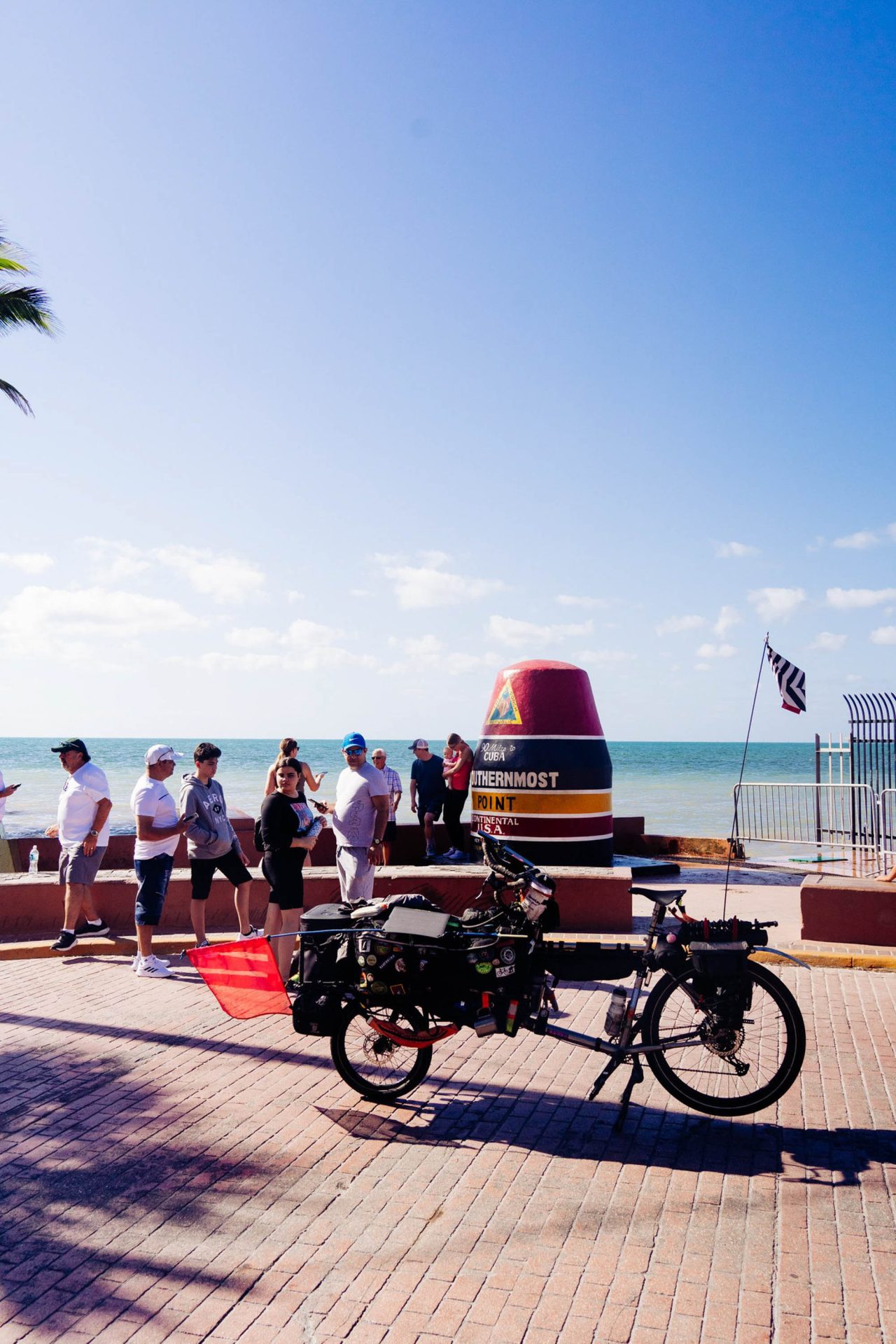 Binggeser's cargo bike parked in Key West, Florida, at the marker for the southernmost point in the continental U.S. A small crowd stands behind the bike, some of them looking at it curiously.