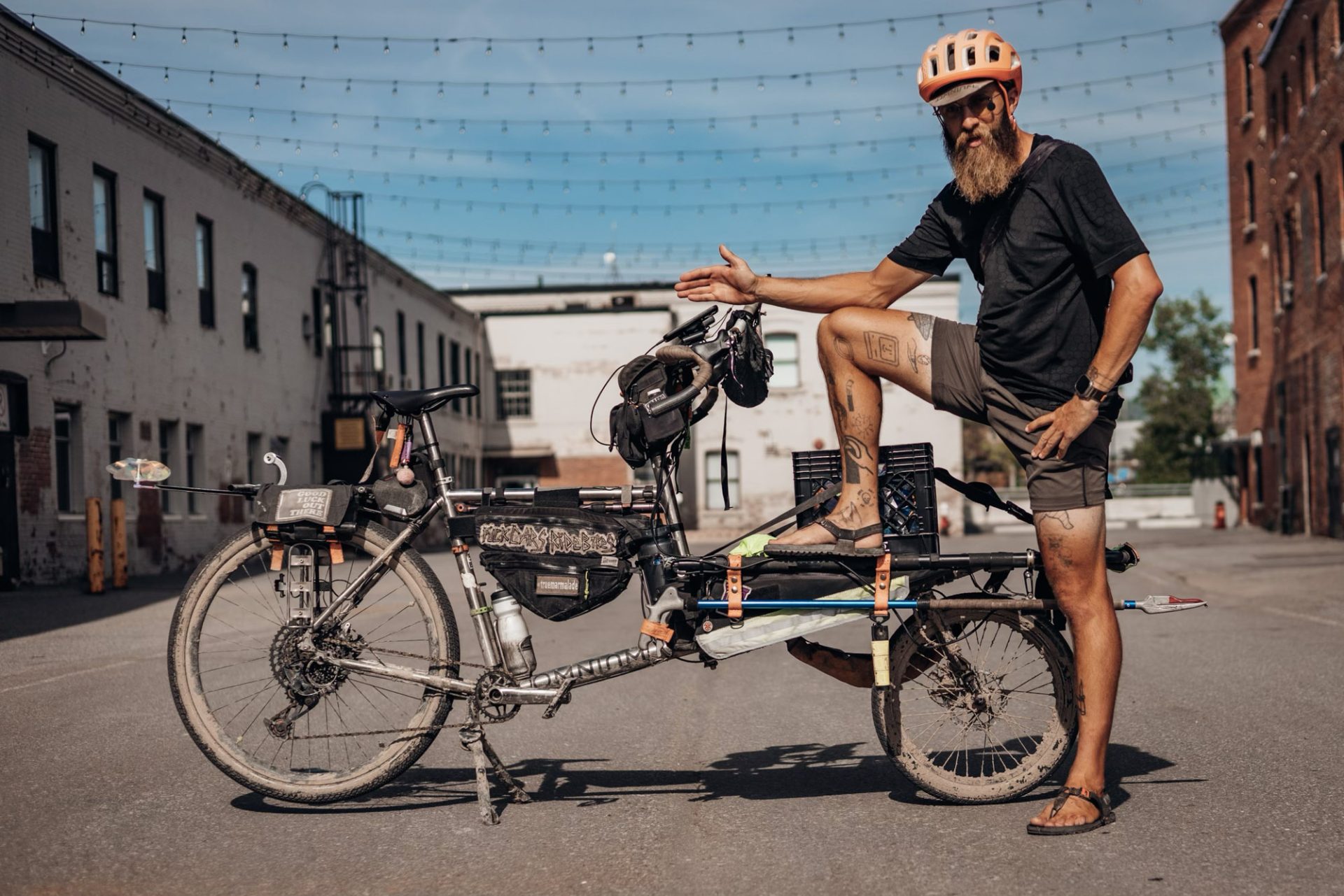 Erik Binggeser stands with his Omnium cargo bike. he's wearing a t-shirt and shorts with sandals and has a long beard.