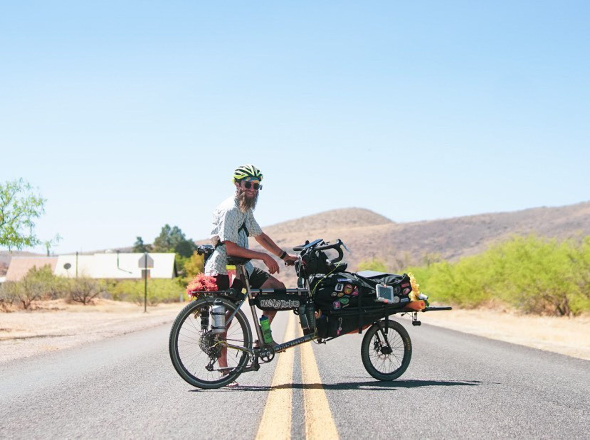 Binggeser poses with his bike, standing in the middle of a road in what looks like a dry, Arizona-desert landscape.