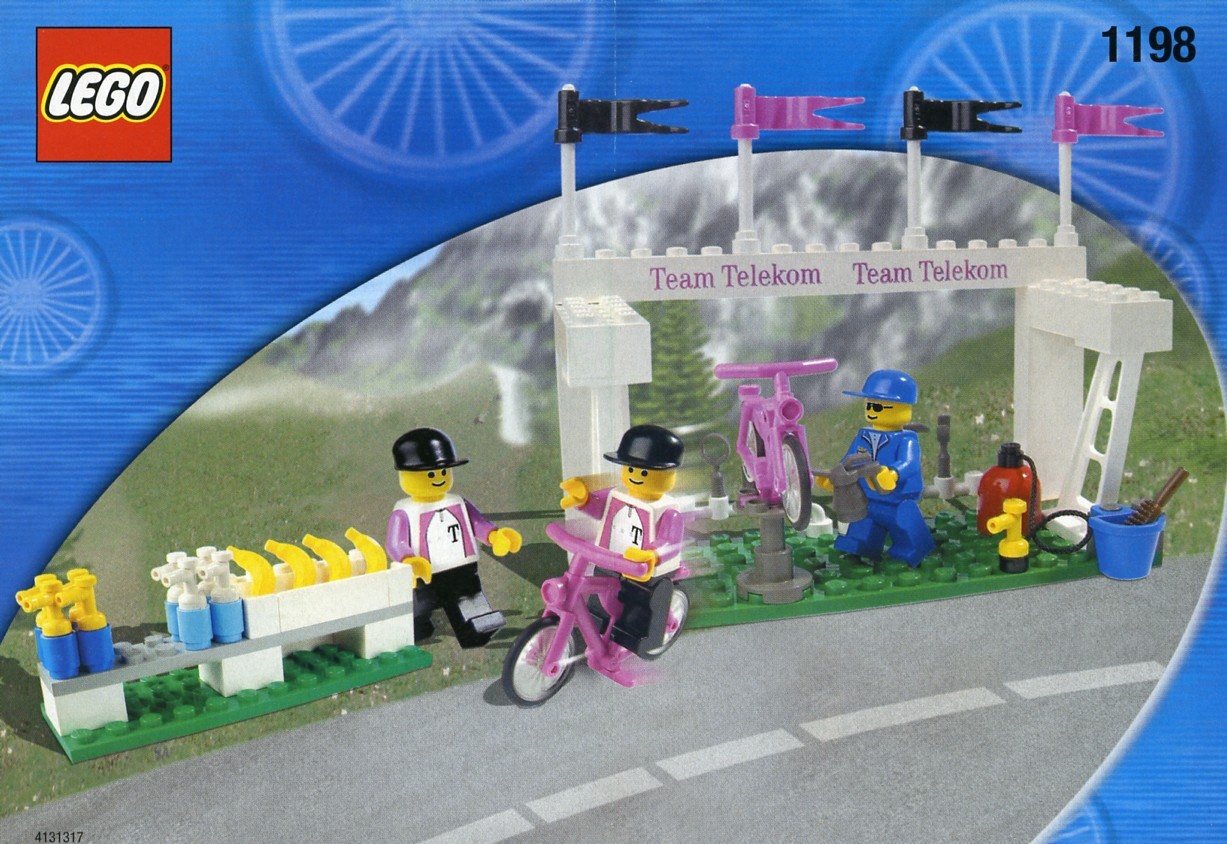 A Lego workshop scene, with a mechanic working on a bike on a stand, a rider zooming past, and a pile of Lego drink bottles and bananas. 
