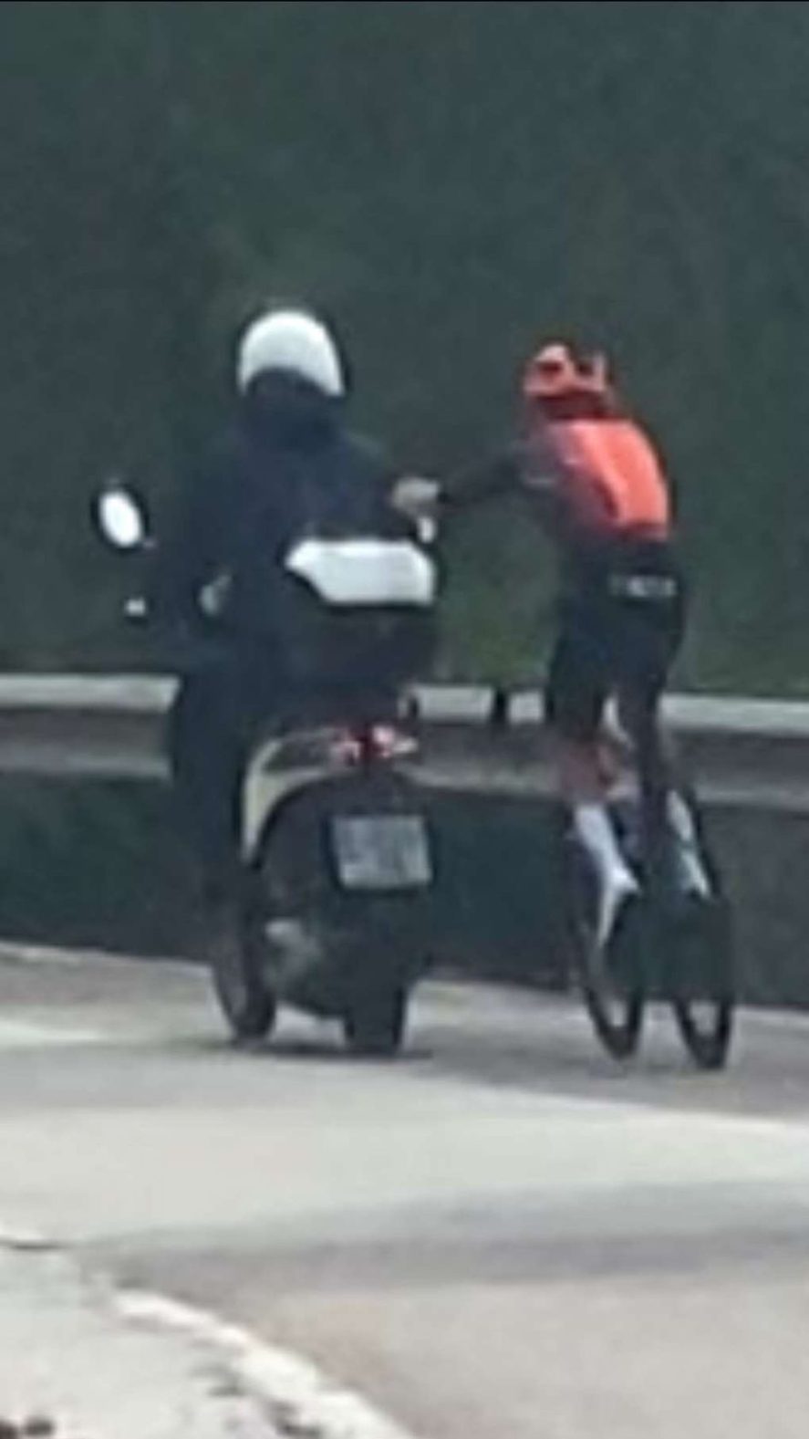 The image shows an Ineos Grenadiers rider holding onto a scooter.