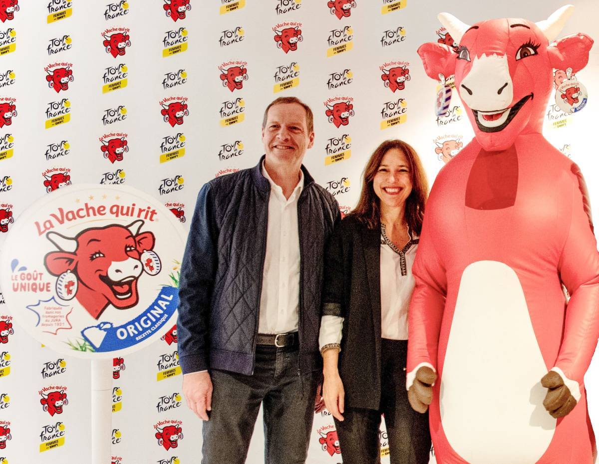 Christian Prudhomme and Anne-Sophie Carrier stand smiling next to a big red cow. Everyone looks very pleased.