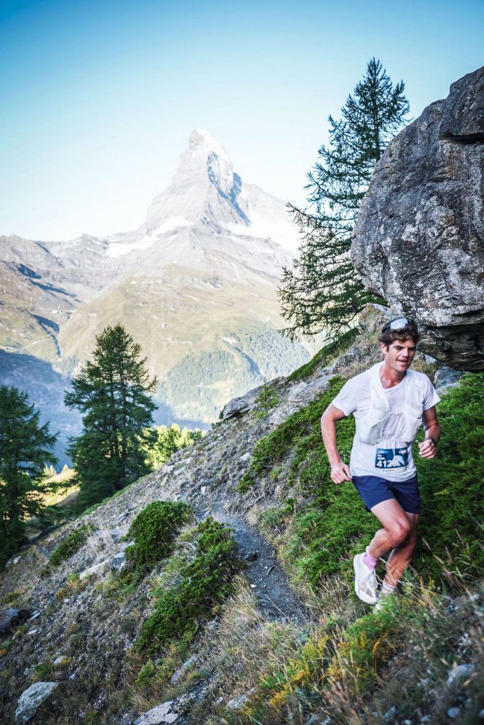 Keir Plaice races on a narrow singletrack trail with the iconic Matterhorn rising in the background. He has a slight smile on his face even as the effort is clear from his sweat-soaked shirt.