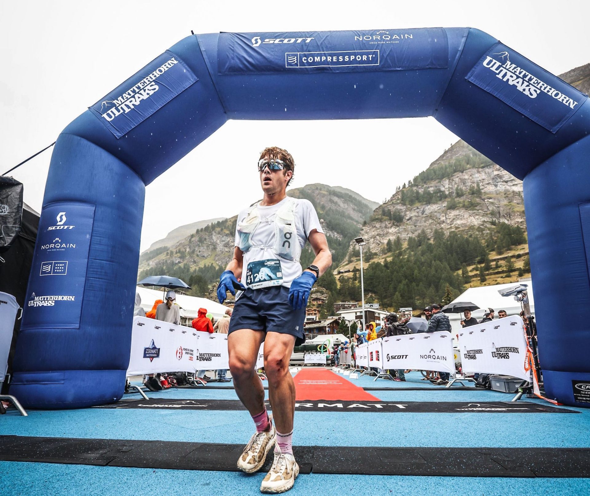 An exhausted Keir Plaice crosses the finish line at the Matterhorn Ultraks. He's the only runner in the frame. His muscled legs are dirty and one knee is bloodied from a fall. His hair hangs limp and sweaty around his face and his mouth is open in an obvious expression of fatigue.