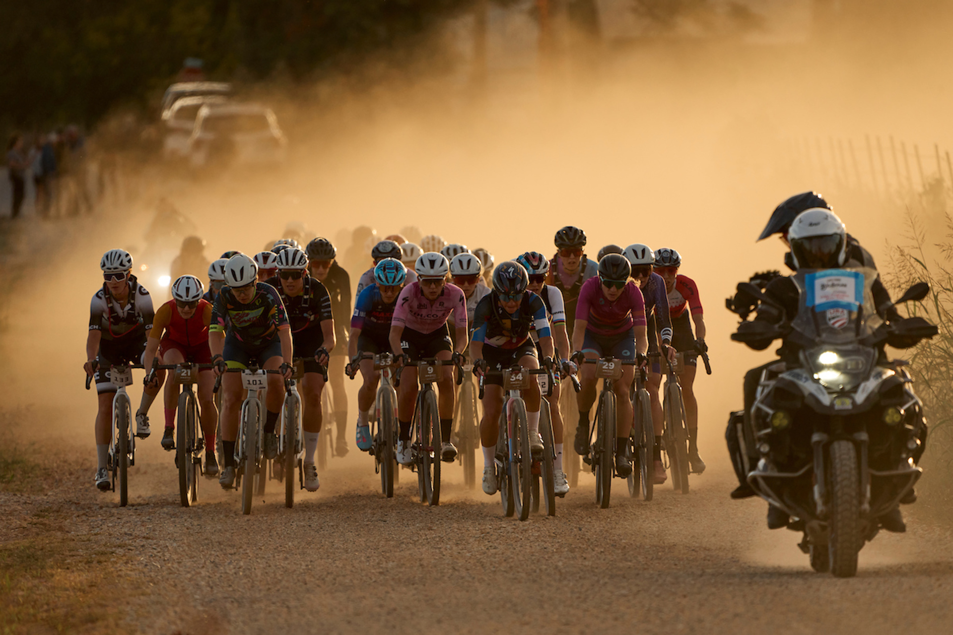 The women's field races at Big Sugar. The light is low and soft, and a pack of riders kicks up a golden cloud of dust behind as a TV moto leads them.