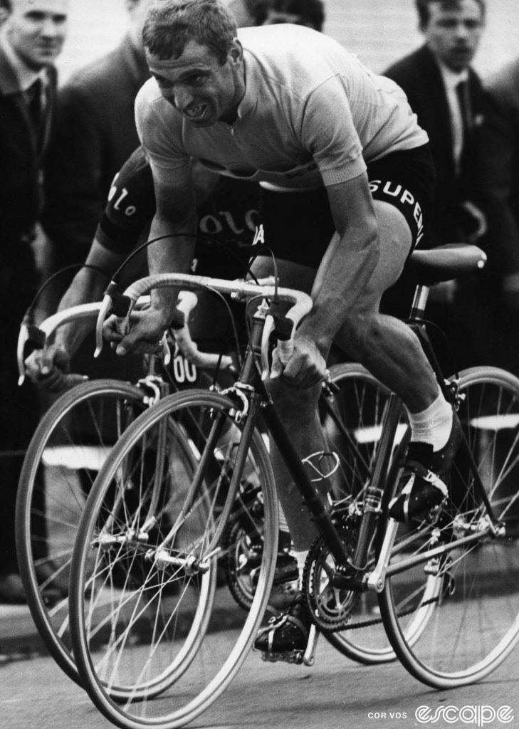 Rik Van Looy sprints out of the saddle in a race in the 1960s. He mostly obscures a rider behind him (to his right) who is vying for the sprint too and appears to be making contact with Van Looy.