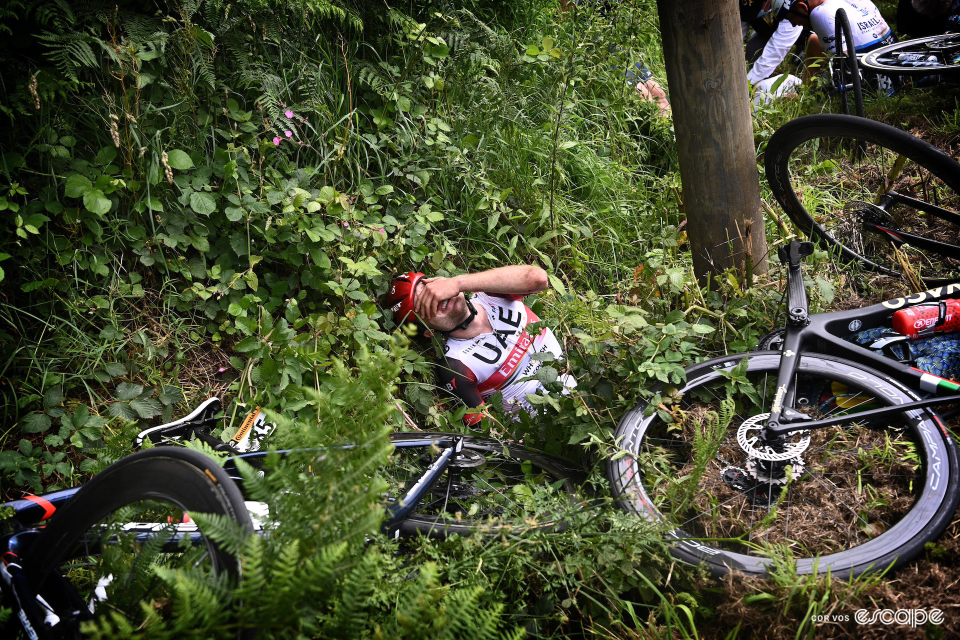Marc Hirschi pictured in a ditch with a hand over his face, visibly in pain, after a crash on stage 1 of the 2021 Tour de France.