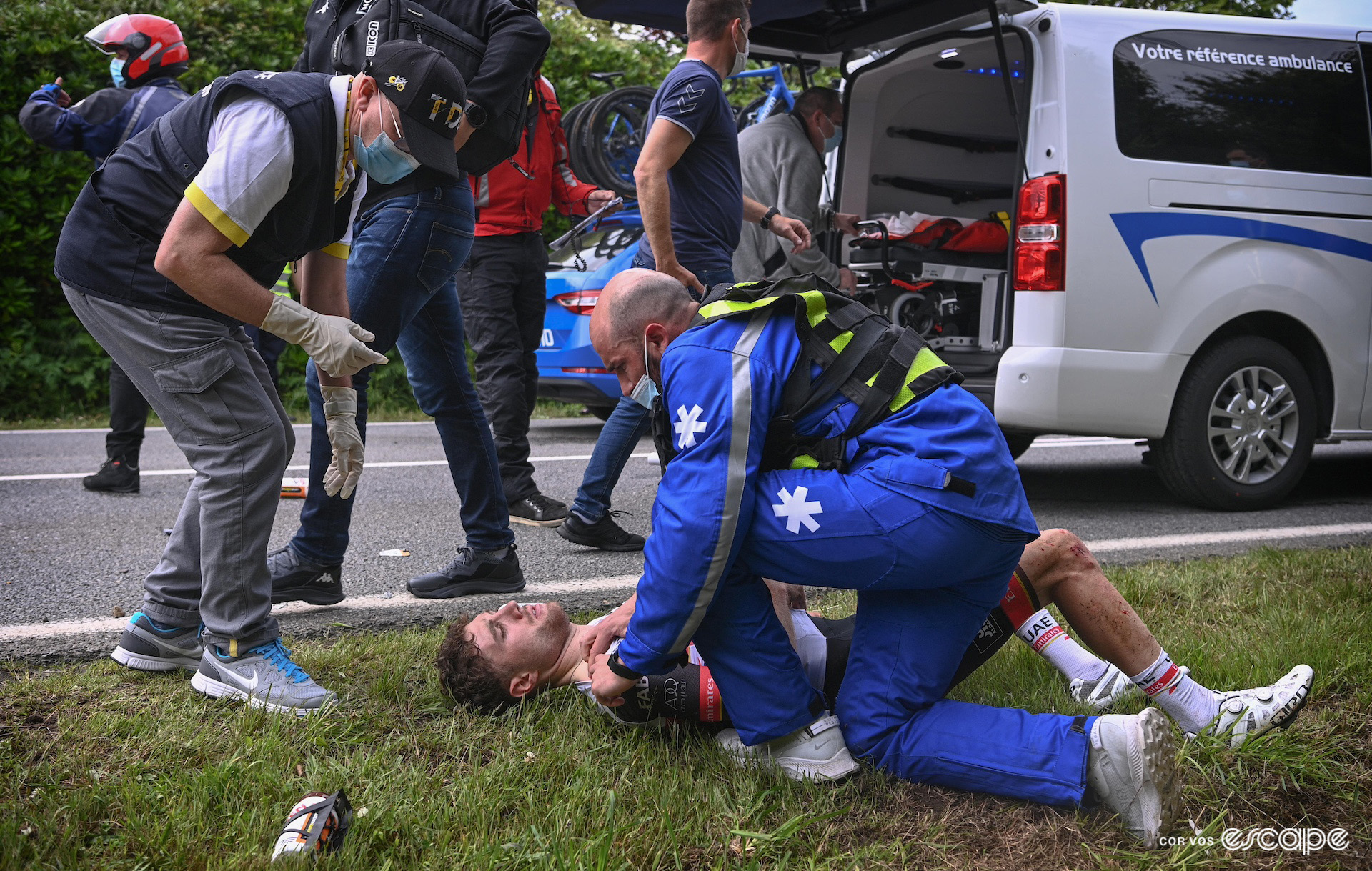 Marc Hirschi pictured lying on his back on the grass verge as he's assessed by a paramedic after a crash on stage 1 of the 2021 Tour de France.