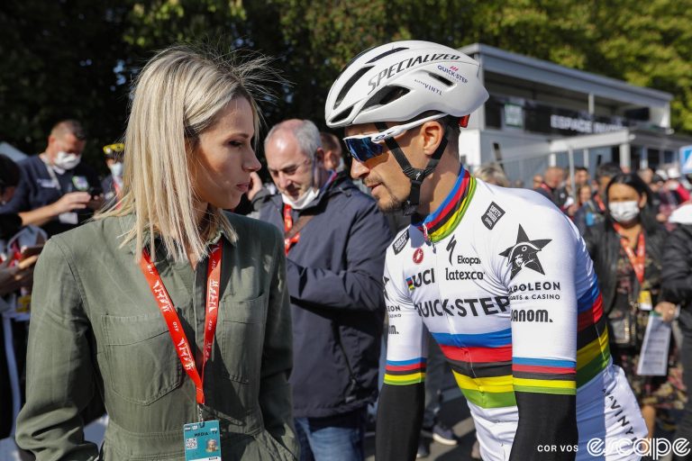 Marion Rousse and her partner Julian Alaphilippe are shown at the start of the 2022 Liege-Bastogne-Liege. She is an accredited media member while he has the rainbow jersey of World Champion.