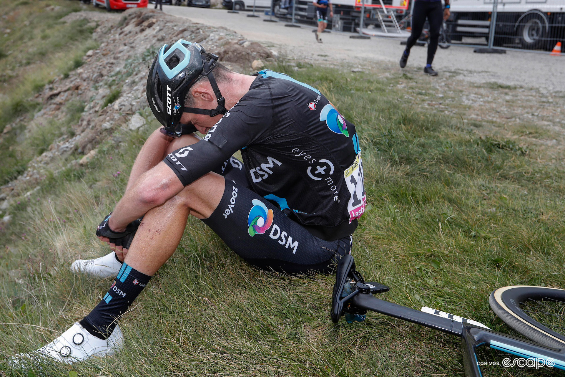 Romain Bardet sits on the grass, head drooping in exhaustion after finishing stage 11 of the 2022 Tour de France on the Col du Granon.