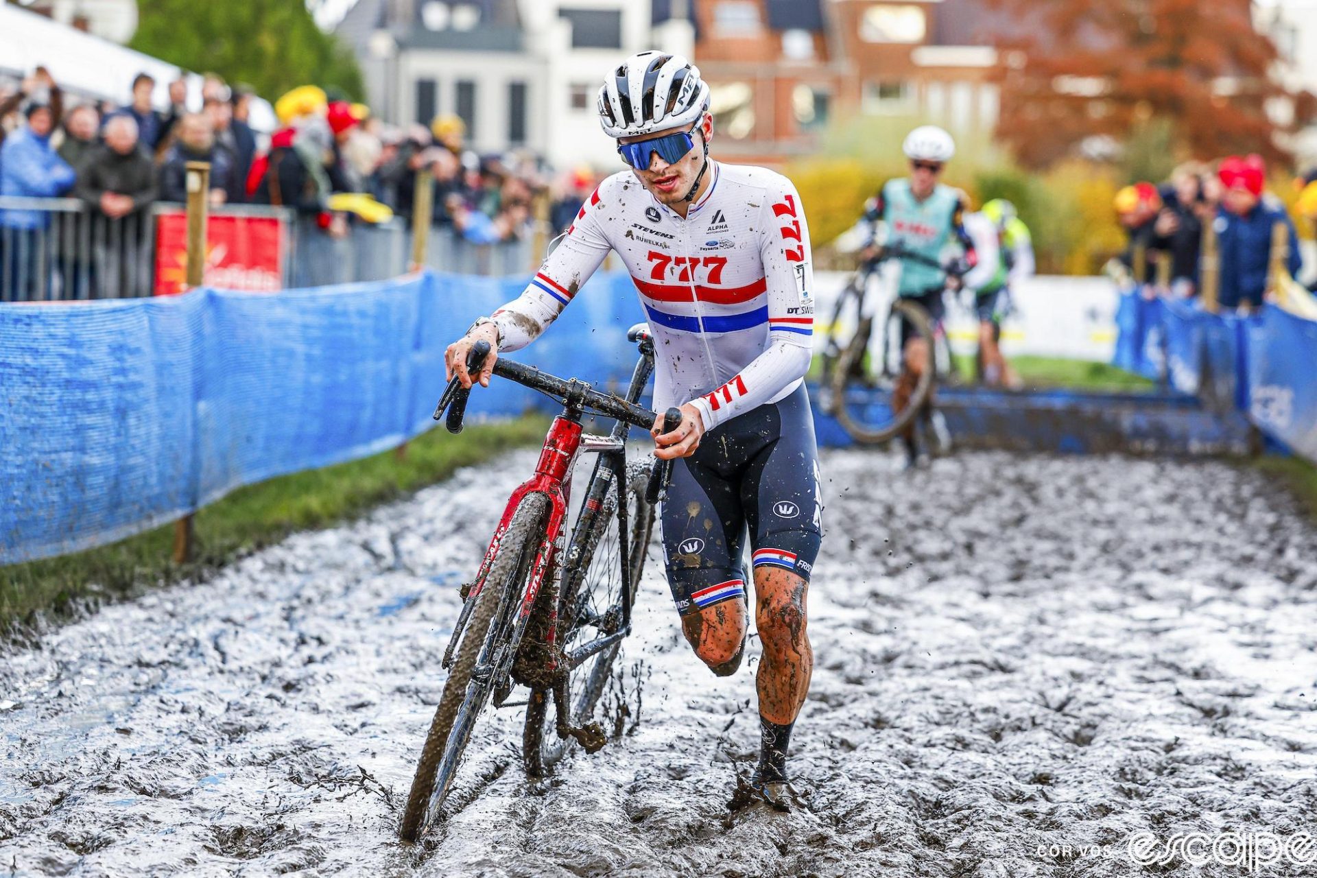 Cameron Mason races through the mud at the X2O round at Kortrijk in 2023. He's running alongside his bike, in near ankle-deep mud. It must be an early lap because his white British champion's kit is still relatively clean.