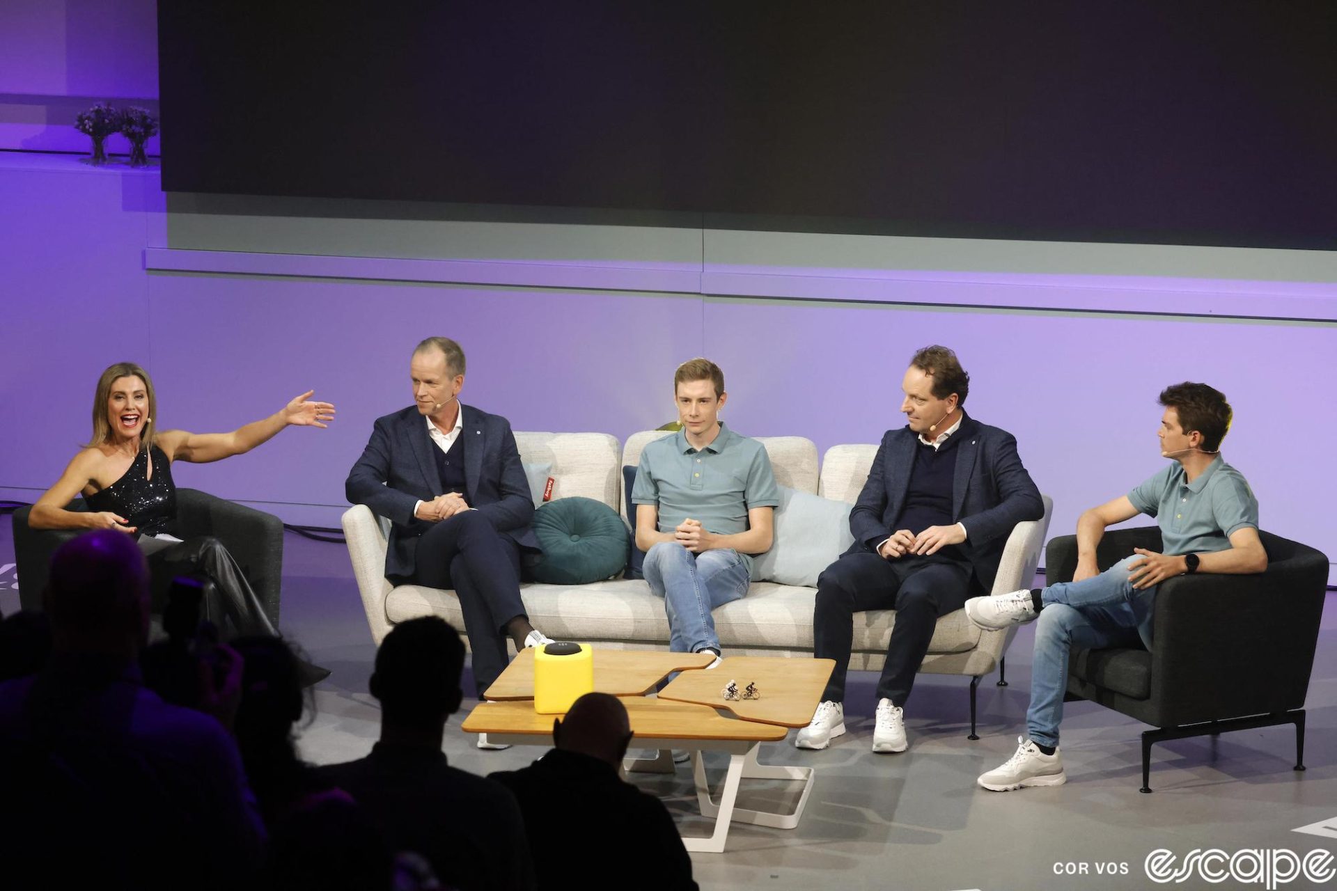 From left to right, Orla Chennaoui, Richard Plugge, Jonas Vingegaard, Merijn Zeeman, and Sepp Kuss sit on chairs and a sofa for a discussion during the Visma team presentation. Kuss looks more relaxed than Jonas, sitting with his left leg crossed over his right, while Jonas' slight frame appears to shrink into the couch slightly.