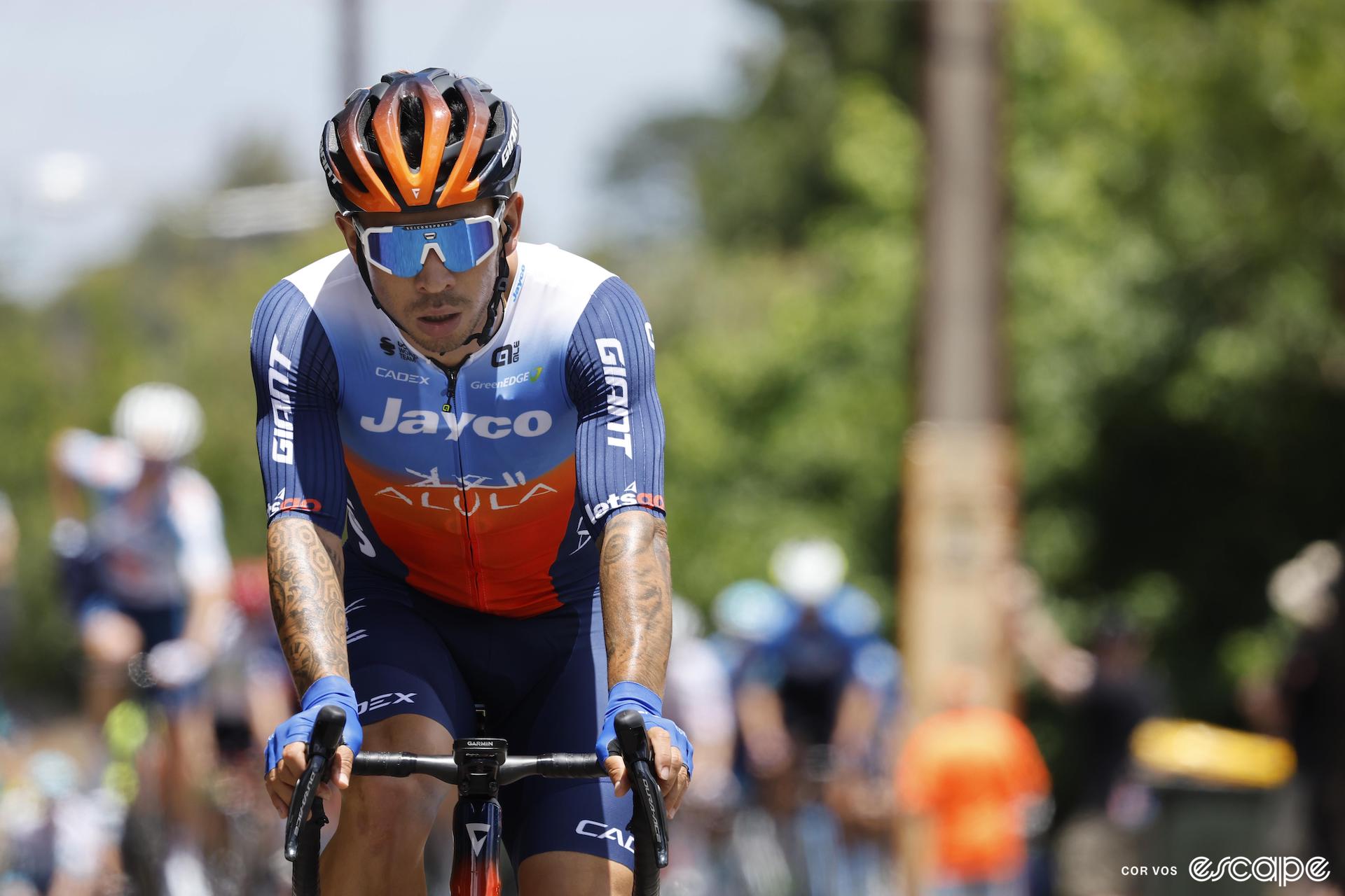A dejected-looking Caleb Ewan rides ahead of a group of riders.