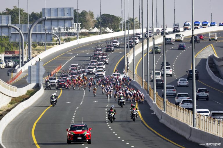 A peloton races along a three lane highway