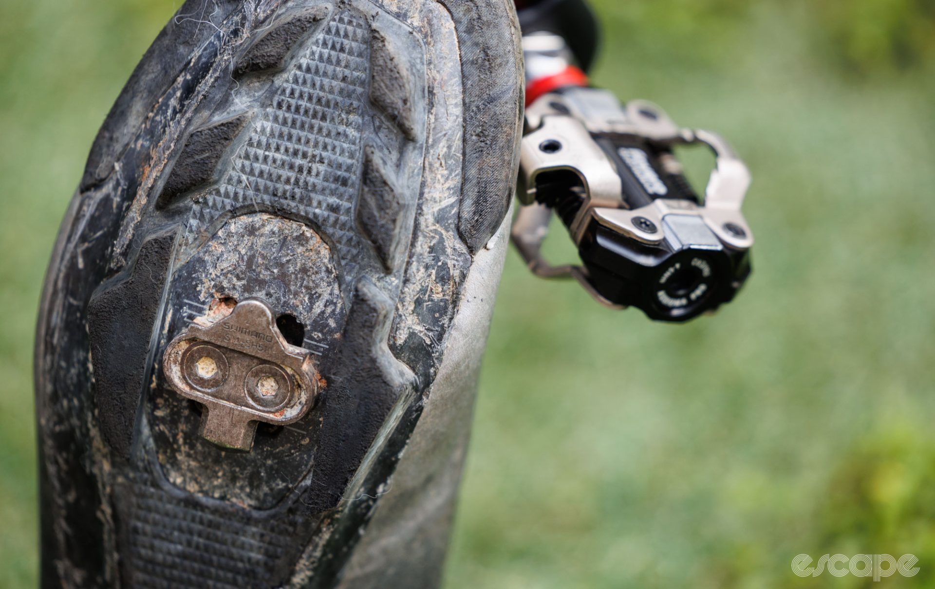 A worn Shimano SPD cleat sits in front of the pedal. 