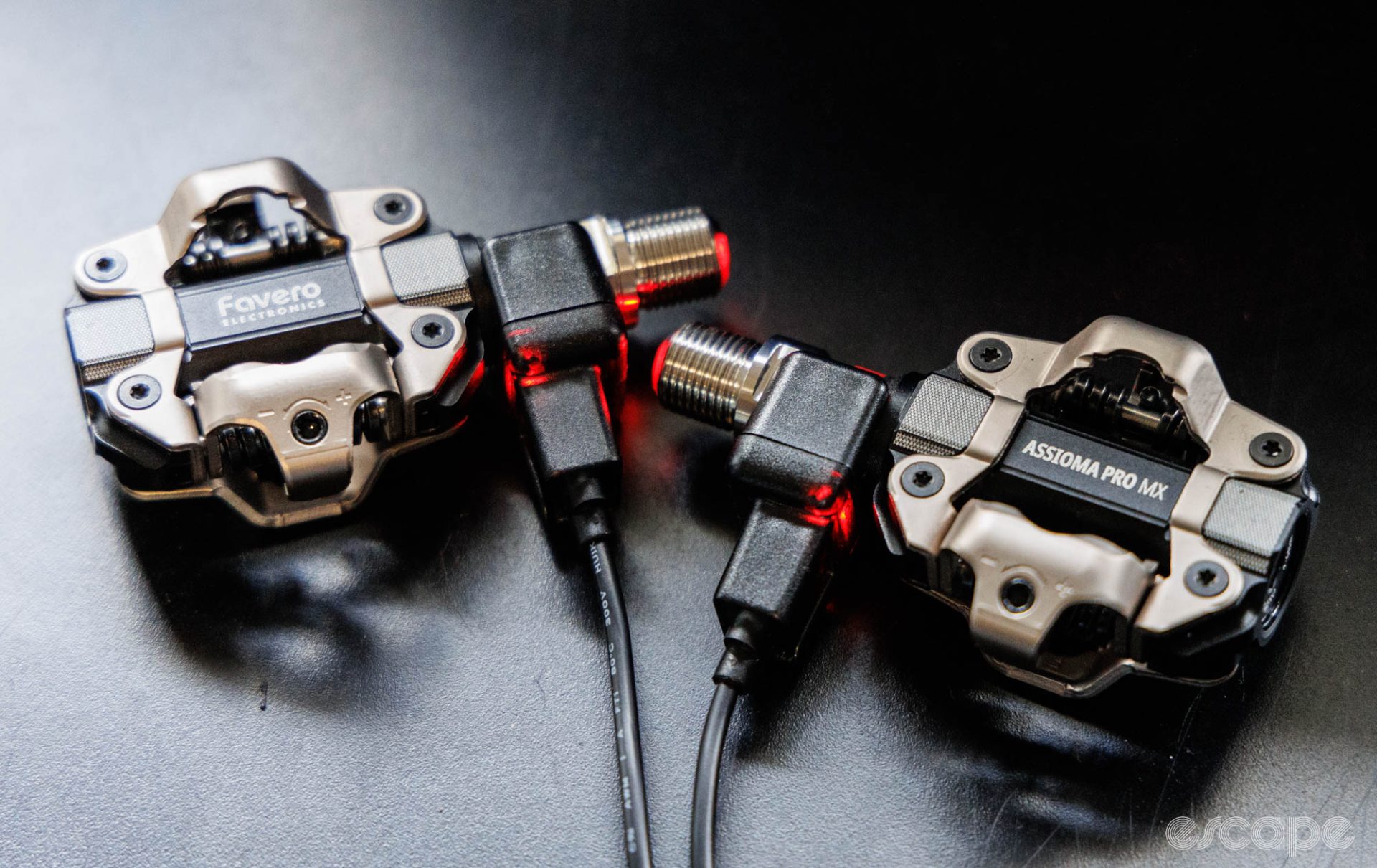 A pair of Favero Assioma Pro MX-2 pedals charging. Red LED indicators show a charge in process. 