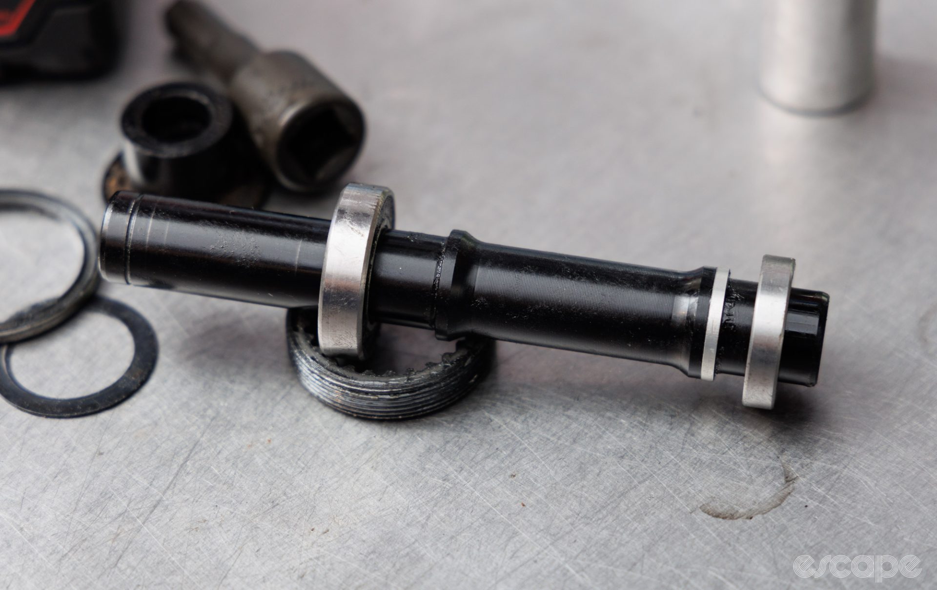 A DT Swiss rear hub axle sits on a bench, with two bearings installed on it. 