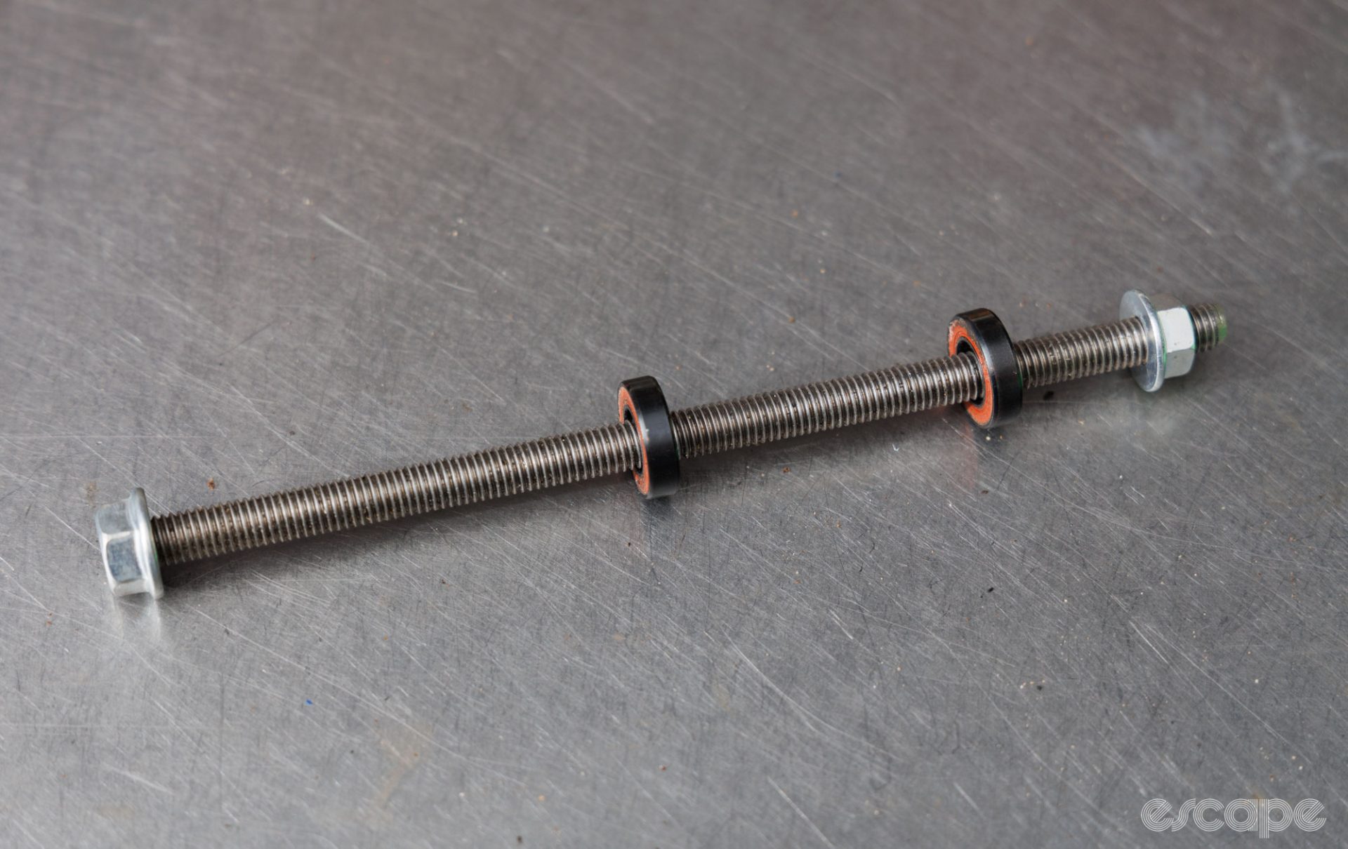 A basic threaded rod, threaded nuts, and some bearings sit on a bench. 