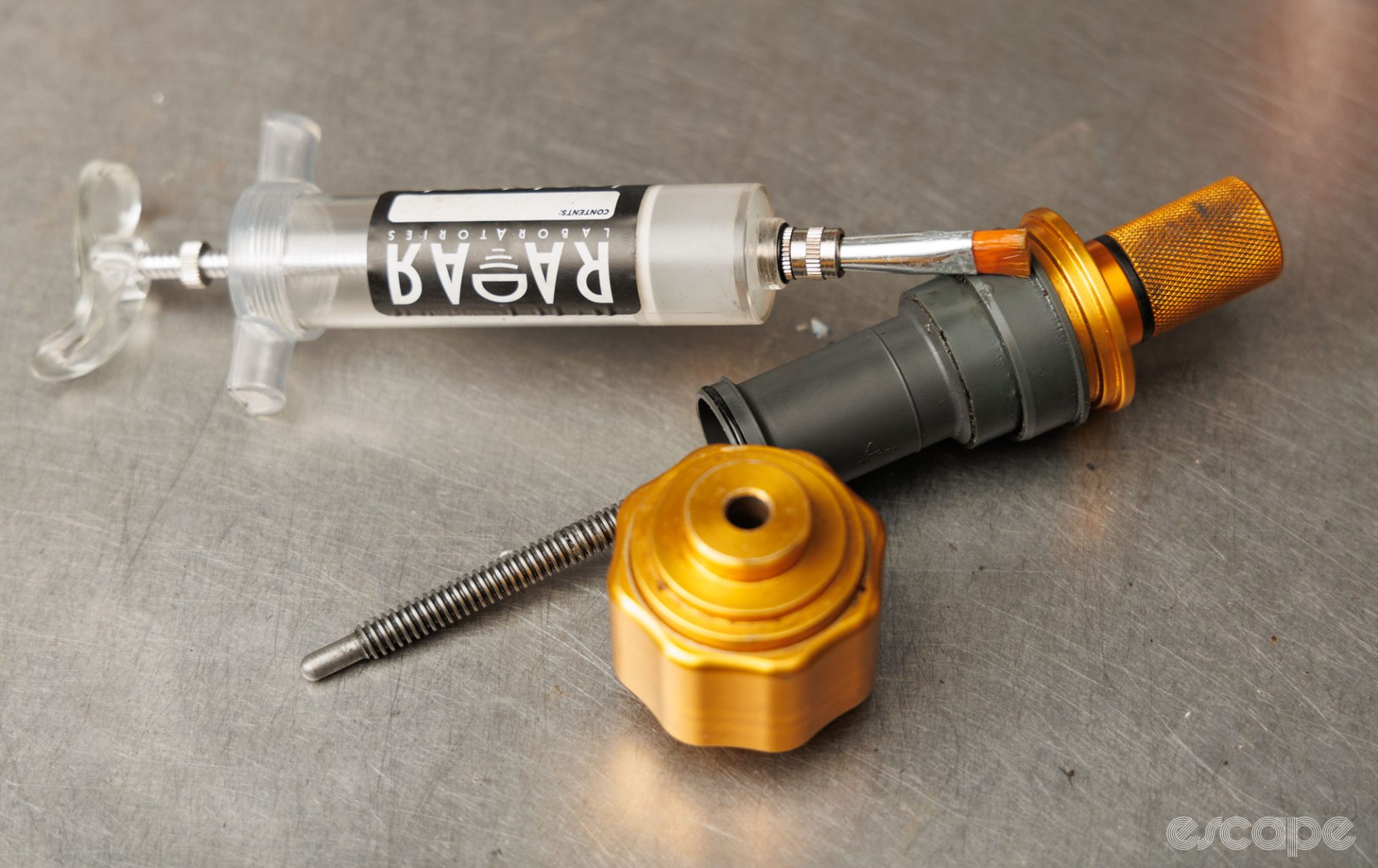 An Enduro bottom bracket tool, Shimano bottom bracket, and a syringe filled with grease sit on a bench. 