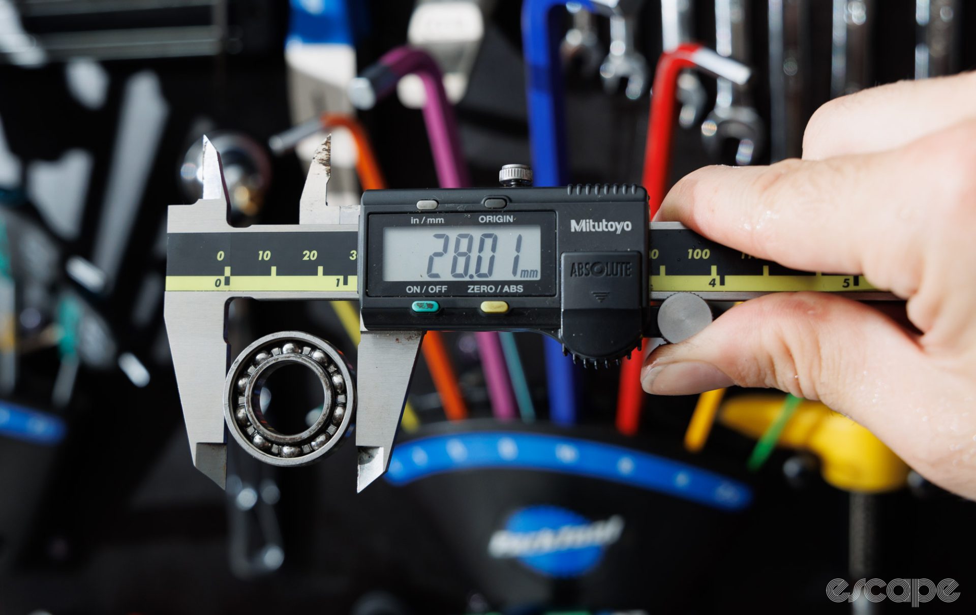 A digital caliper measures the outside diameter of a bearing. The calipers show 28.01 mm. 