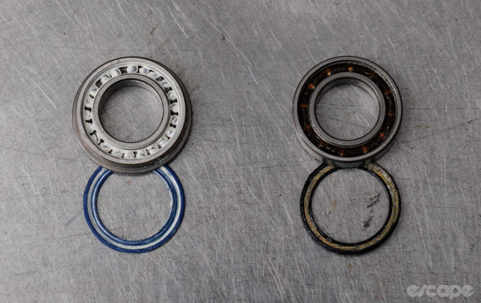 Two bearings, each with one seal removed. On the left is a full complement bearing that is packed tightly with ball bearings. On the right is a more regular bearing, where each bearing is clearly distanced via the use of a ball bearing retainer. 