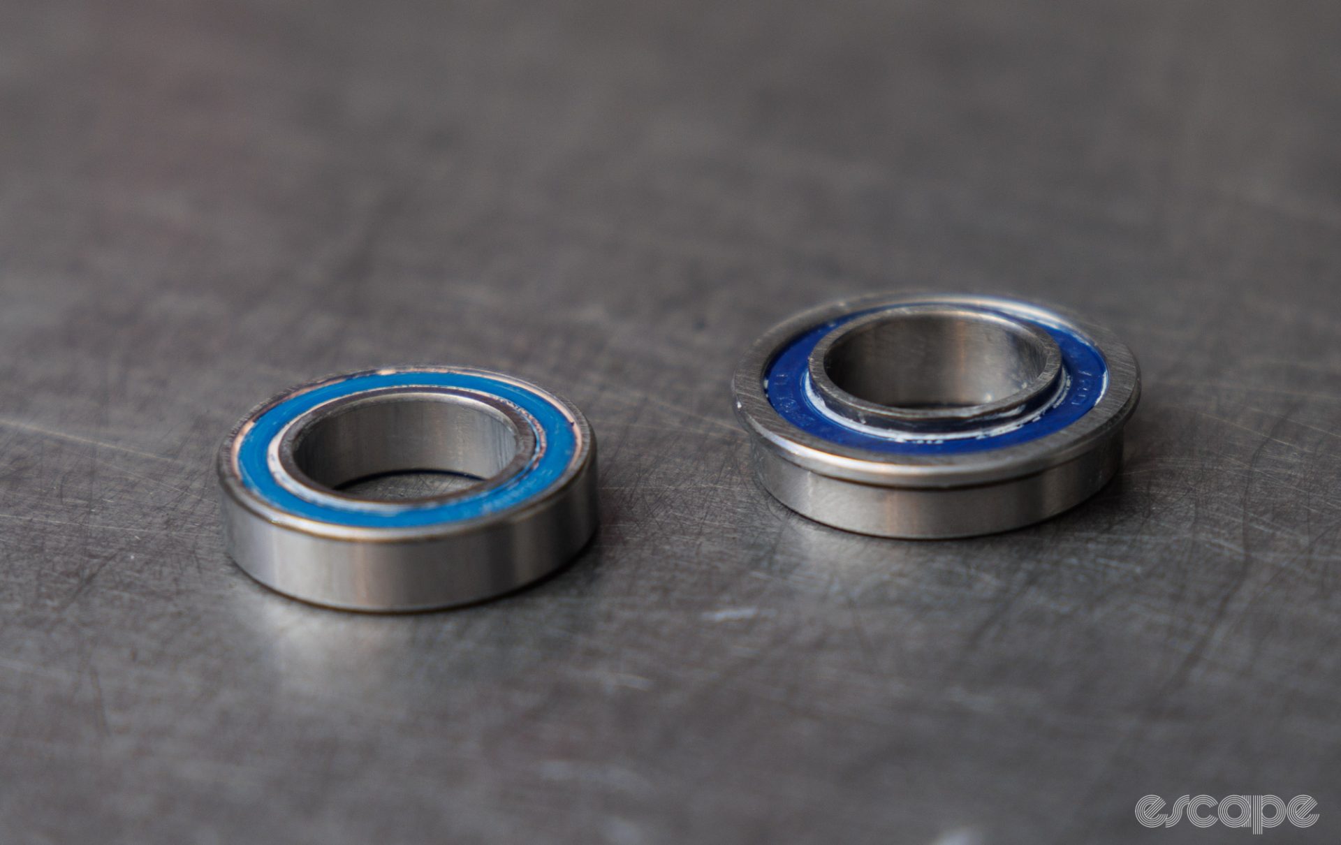 Two new bearings sit next to each other. One is of a standard shape, while the one on the right features an extended inner race and a flanged outer race. 
