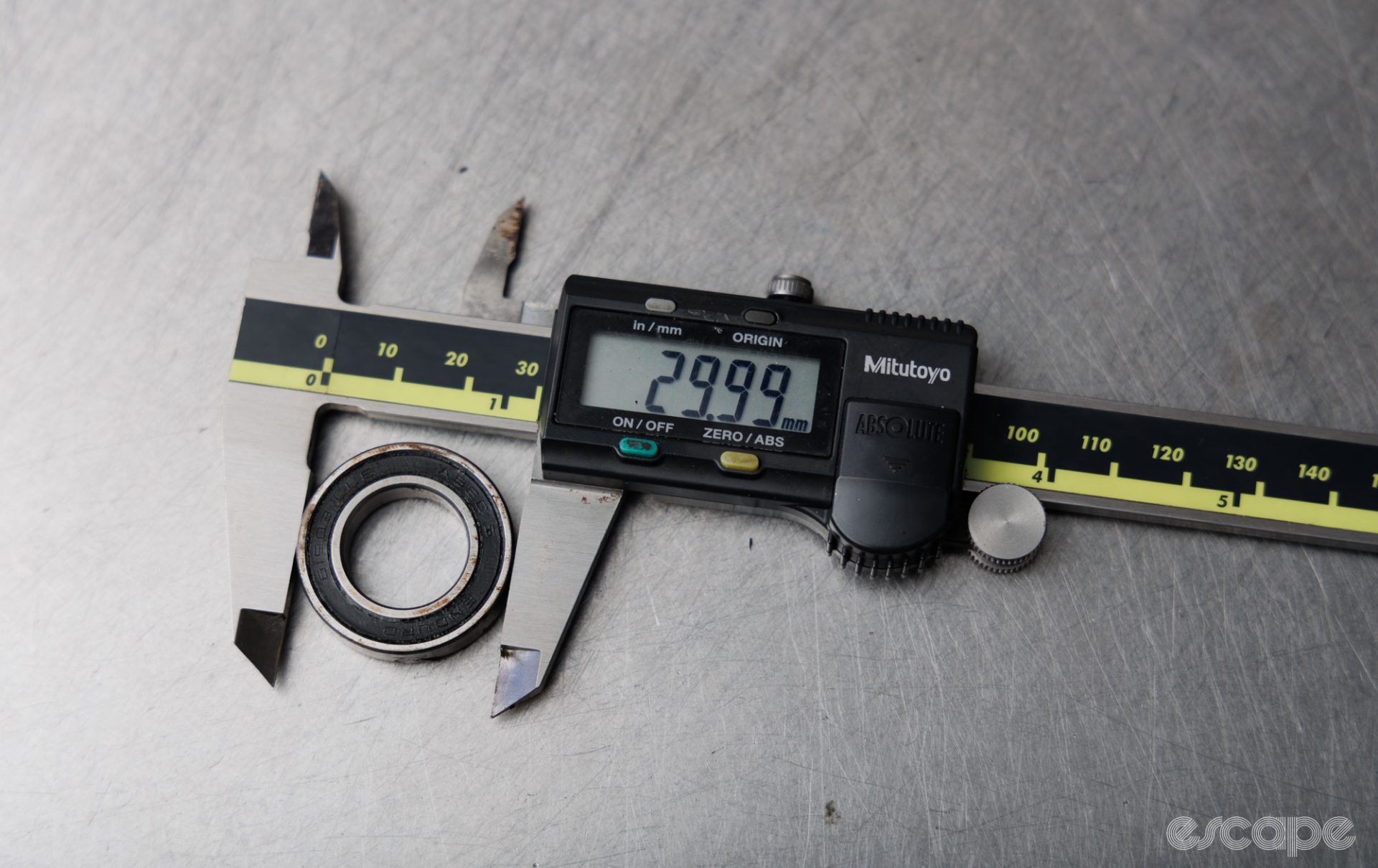 The outer diameter of a cartridge bearing is measured with digital calipers. The calipers read 29.99 mm. 