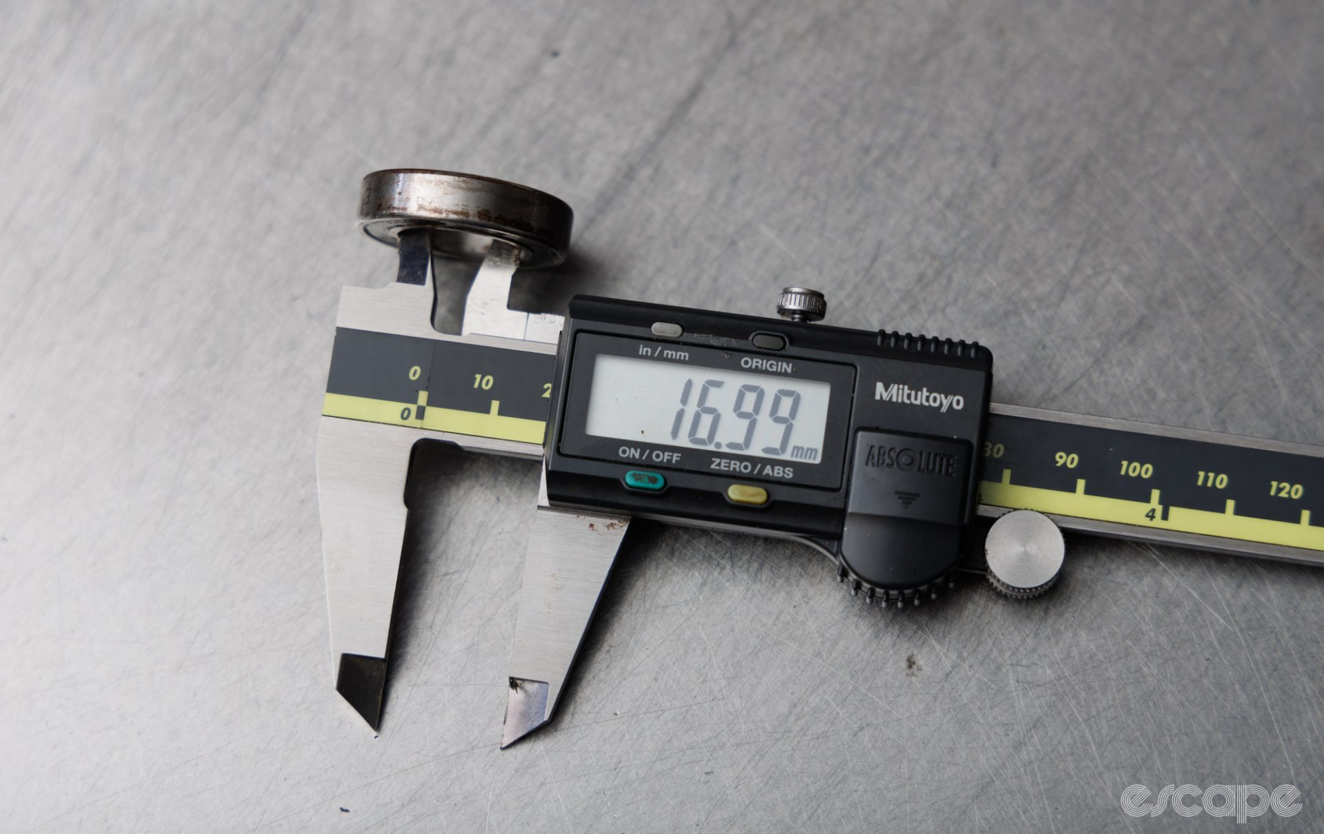 The inner diameter of a cartridge bearing is measured with digital calipers. The calipers read 16.99 mm. 