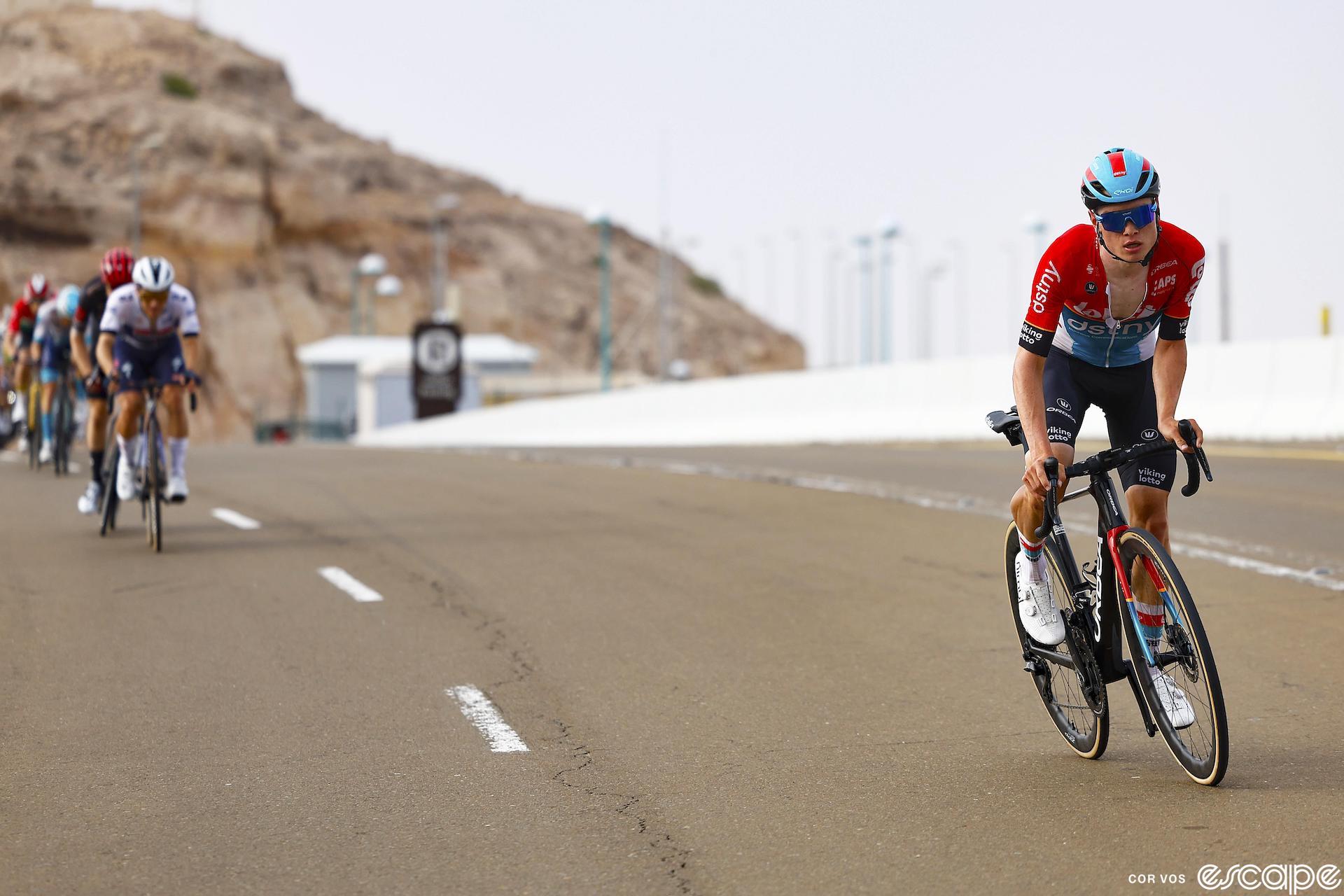 Lennart Van Eetvelt climbs Jabel Hafeet at the 2024 UAE Tour. He's out of the saddle and off the front; roughly 10 meters behind, a Jayco-AlUla rider leads a line of riders trying to close the gap.