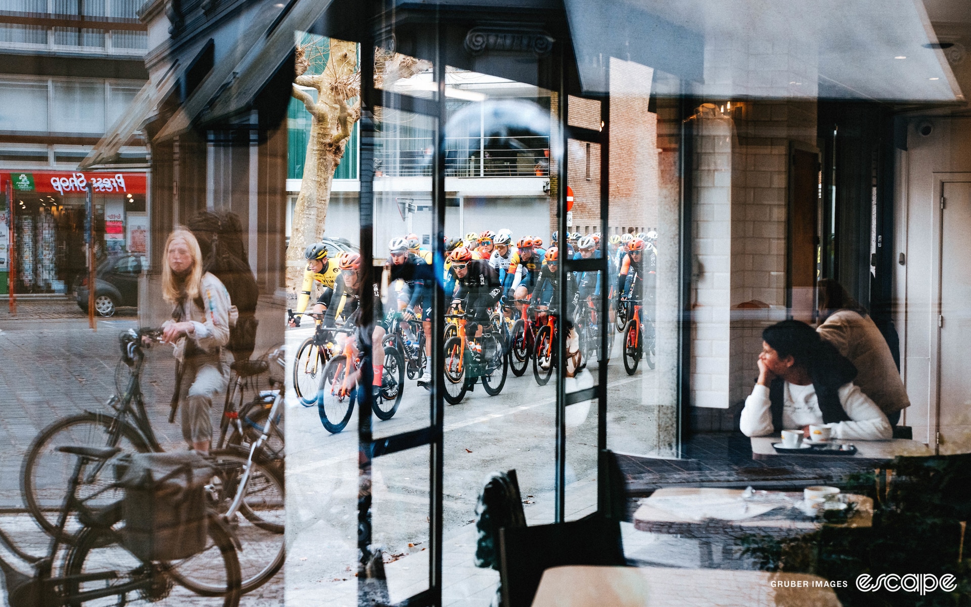 A peloton rides along, as seen from inside a cafe.